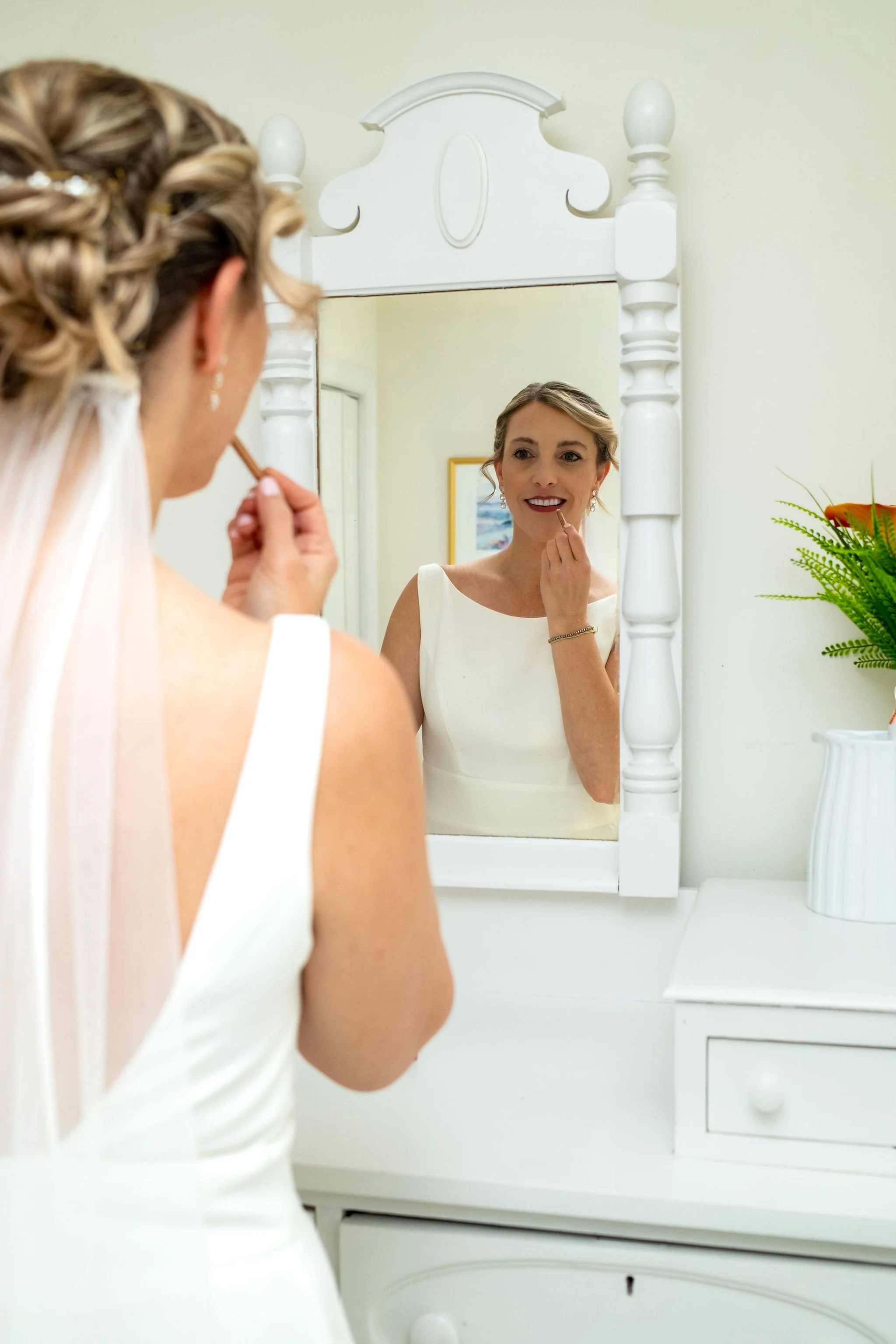 Alli Baudoin applying lipstick in a white vanity mirror while getting ready at a private residence in Mount Desert Maine spring wedding photography VMG Productions