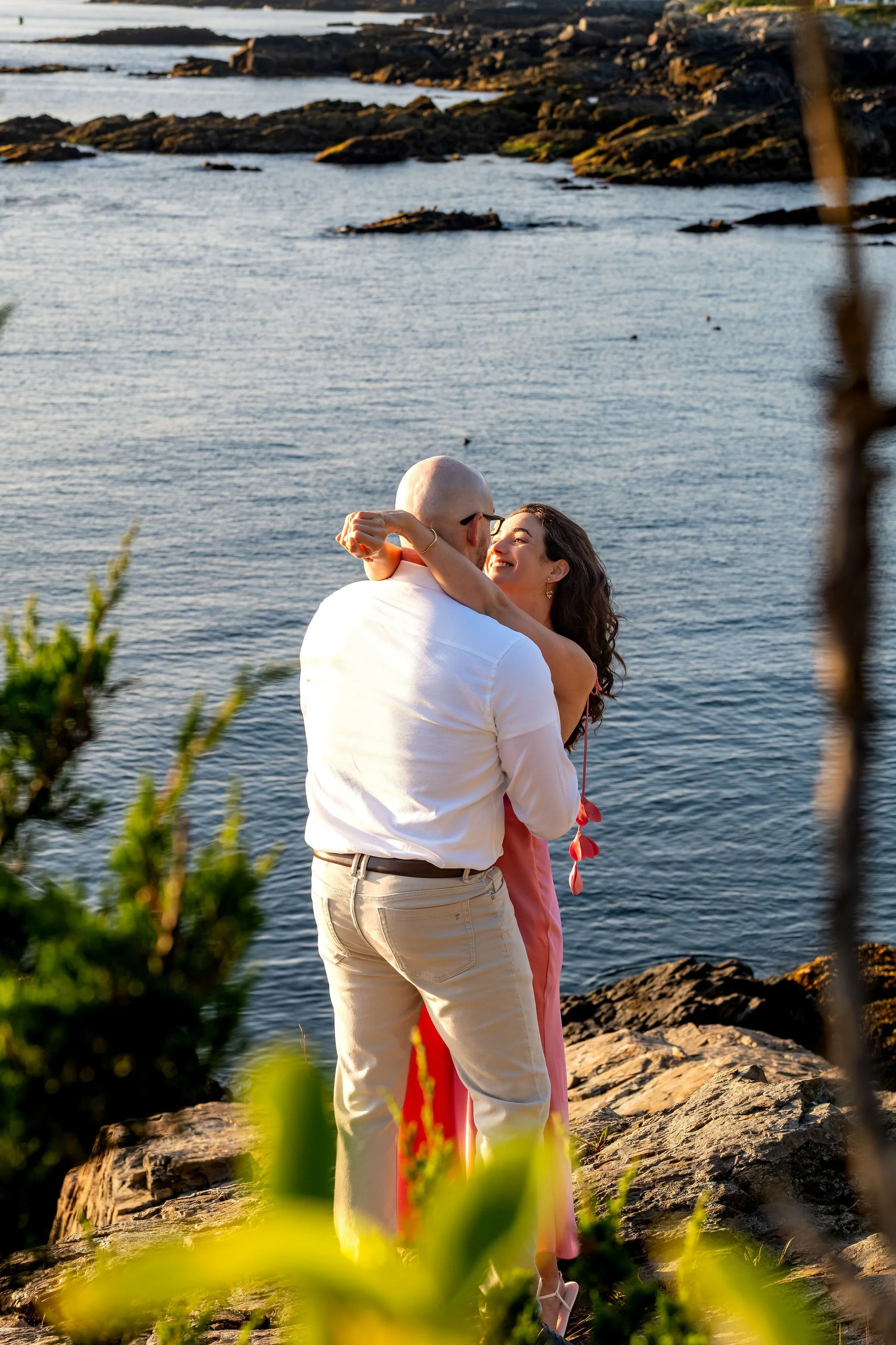 Zack and Helena hugging on the rocks above the calm blue water on Marginal Way in Ogunquit Maine sunrise proposal and engagement photography VMG Productions