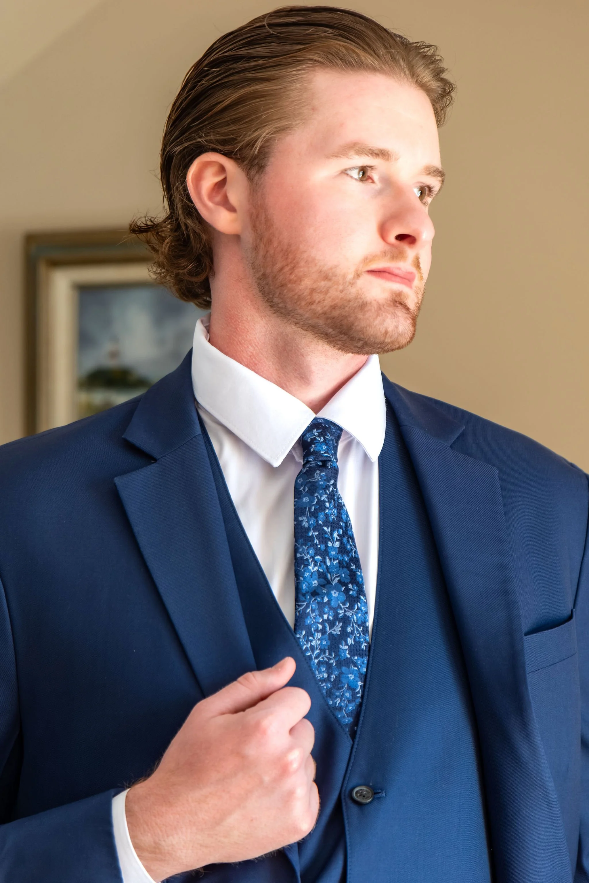 Zachary in a navy three piece suit and floral tie looking off to the side while getting ready at The Lucerne Inn in Dedham Maine summer wedding photography VMG Productions