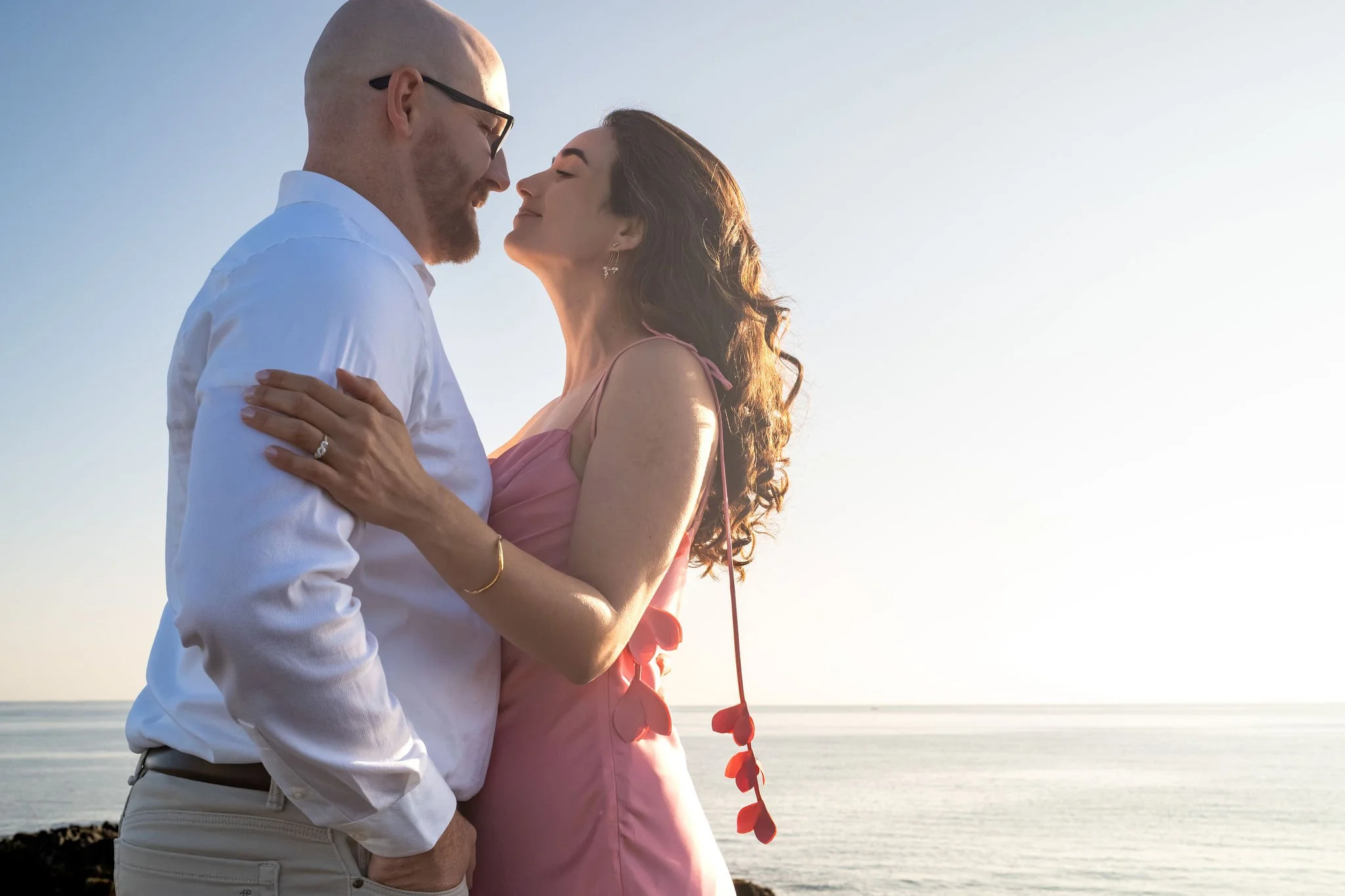 Zack and Helena nose to nose about to kiss with the ocean horizon behind them on Marginal Way in Ogunquit Maine sunrise proposal and engagement photography VMG Productions
