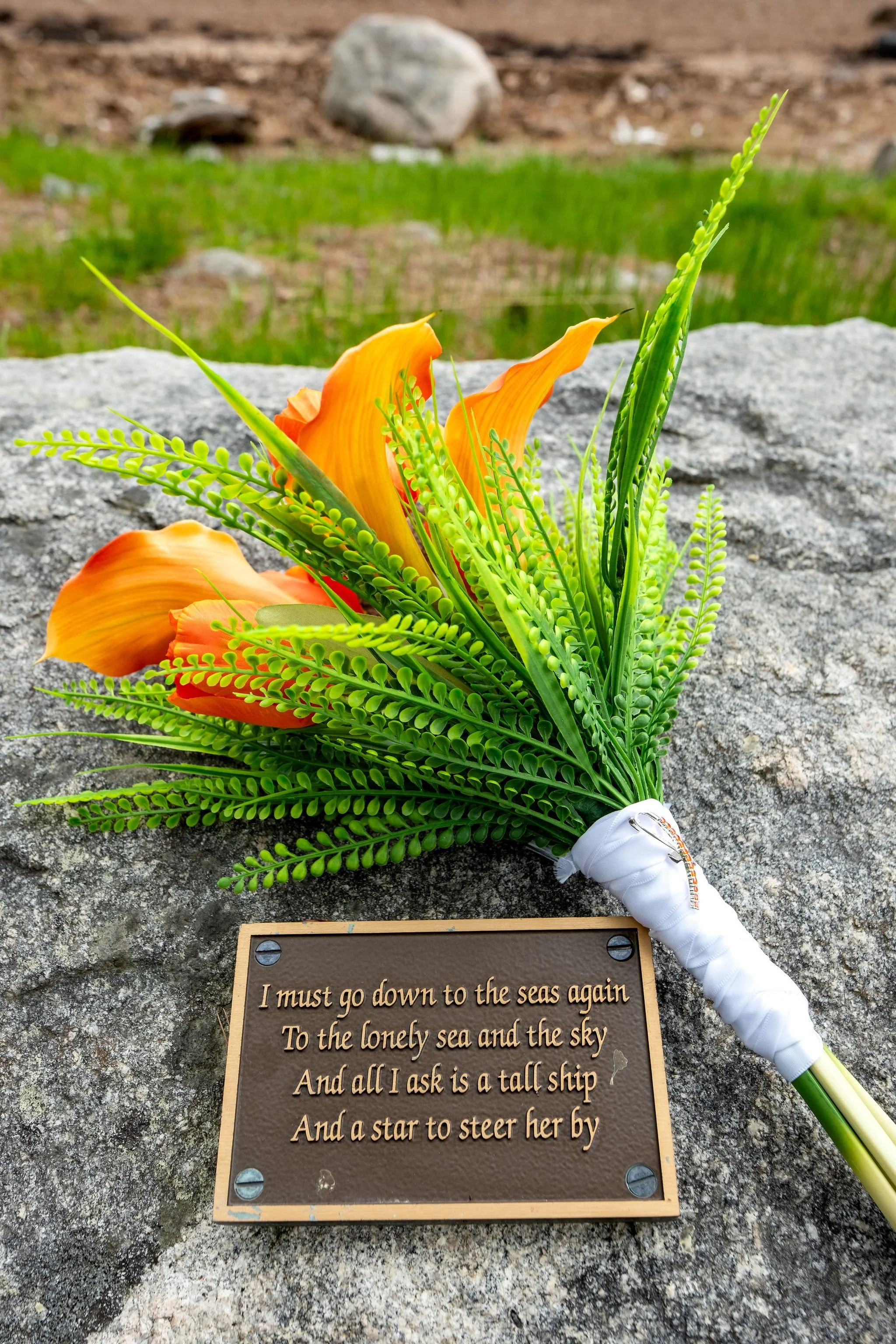 Orange calla lily bouquet resting on a granite ledge beside a bronze sea poetry plaque at the Somes Sound shoreline in Mount Desert Maine spring wedding photography VMG Productions