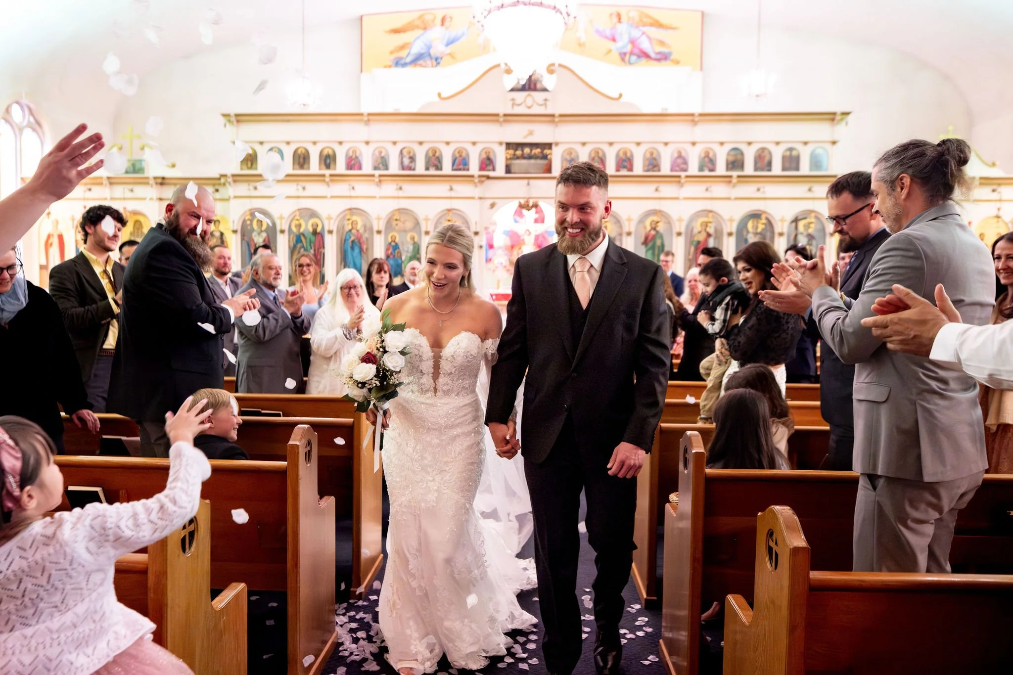 Jeremiah and Vienna walk down church aisle while guests celebrate and toss flower petals at Holy Trinity Greek Orthodox Church Portland Maine spring wedding photography VMG Productions