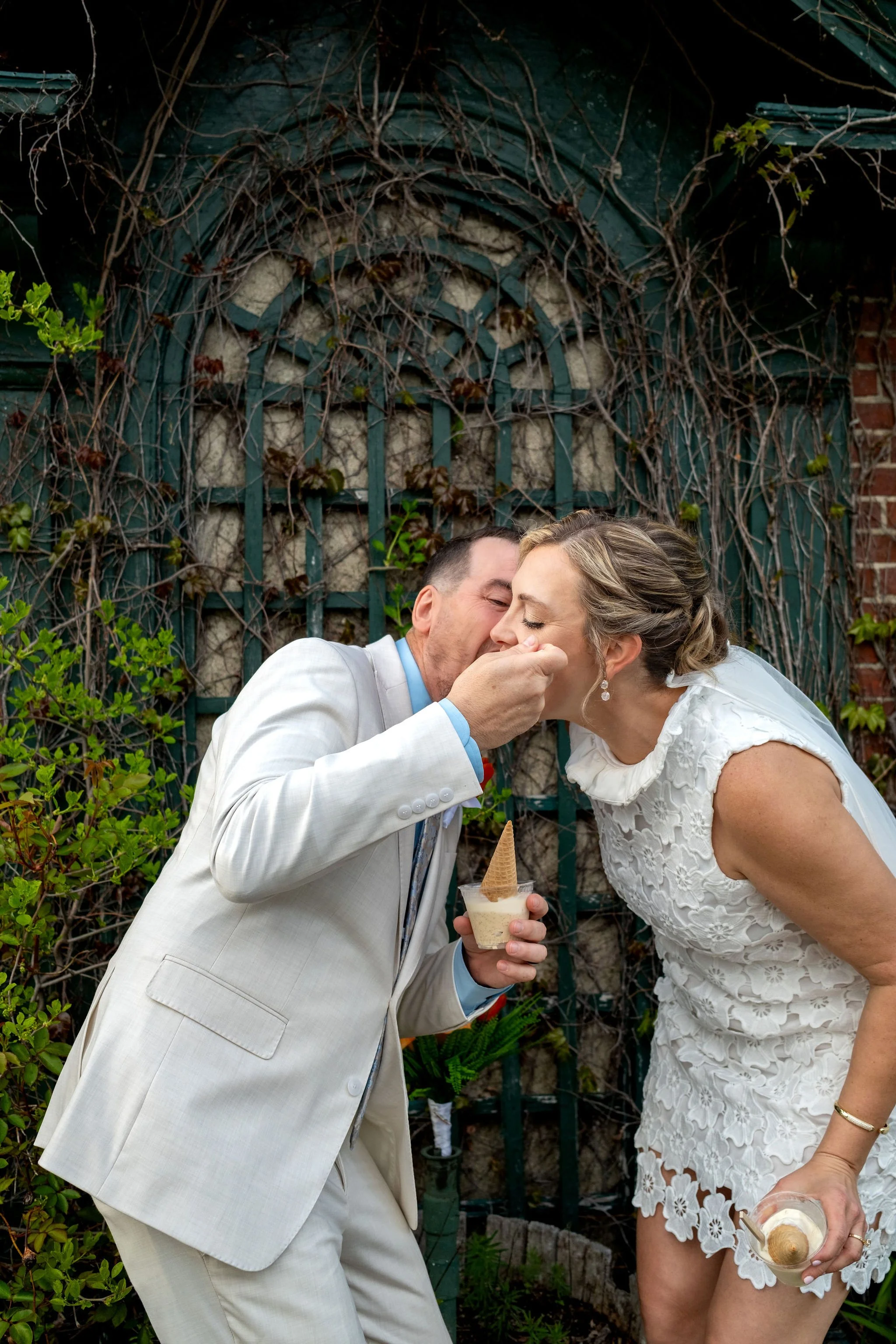 Adam Baudoin feeding Alli a bite of ice cream in front of the green trellis arch in Bar Harbor Maine spring wedding photography VMG Productions