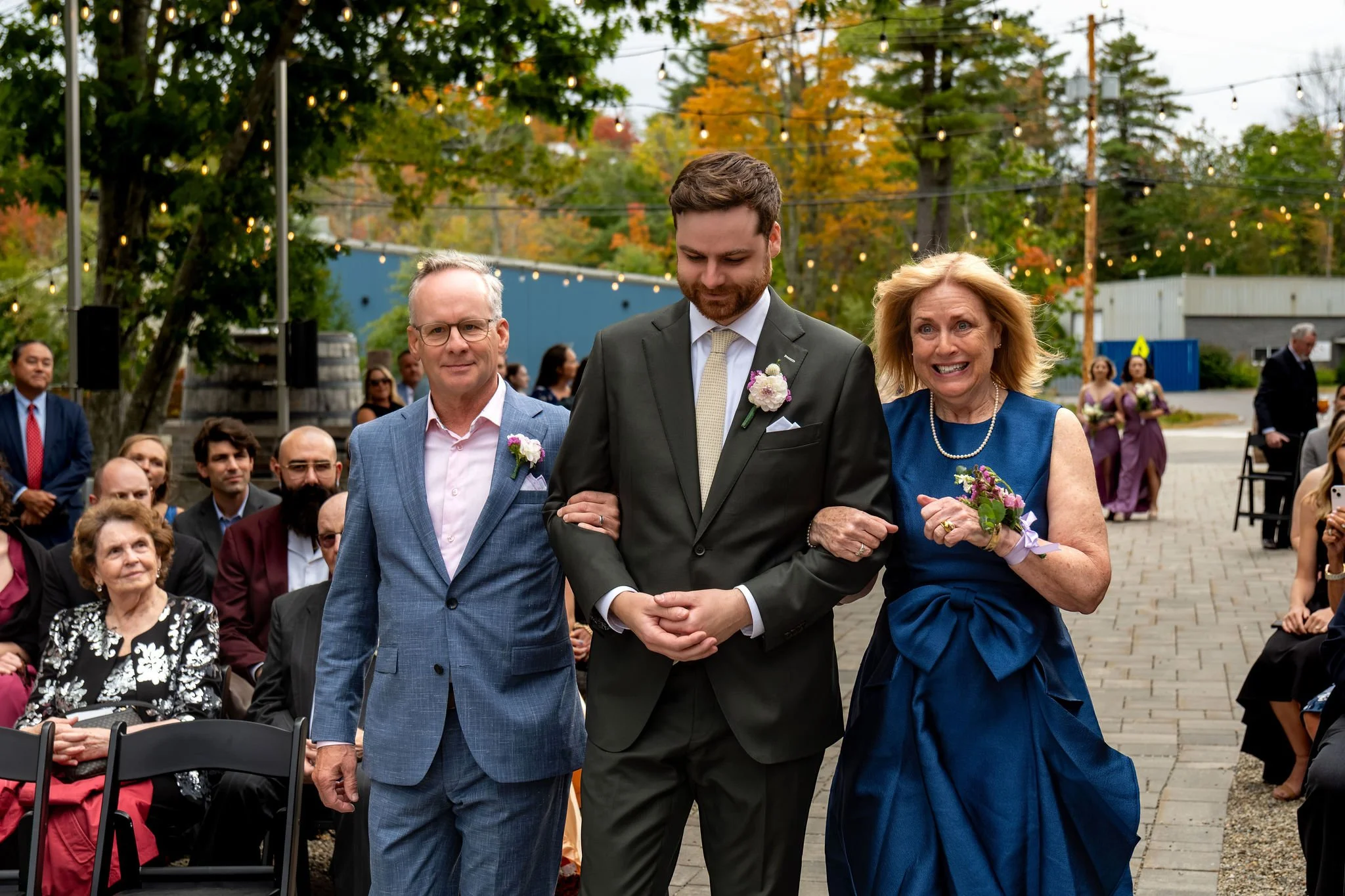 Jack walking down the aisle arm in arm with his mom and dad as guests look on at The Cellars at Allagash Brewing Company in Portland Maine fall wedding photography VMG Productions