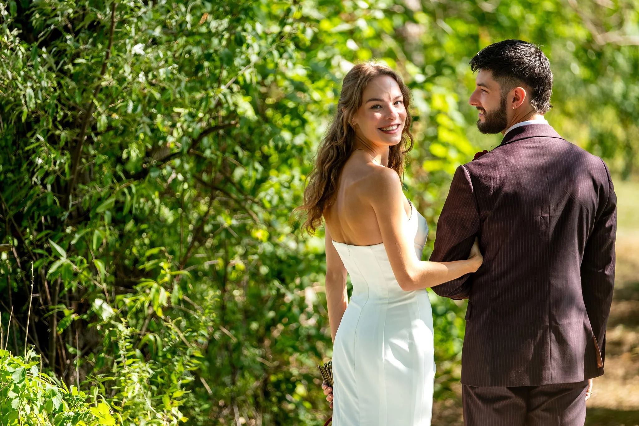Cassidy Begin looking back over her shoulder while walking a wooded trail with Chase at Maple Hill Farm Inn and Conference Center in Hallowell Maine summer wedding photography VMG Productions