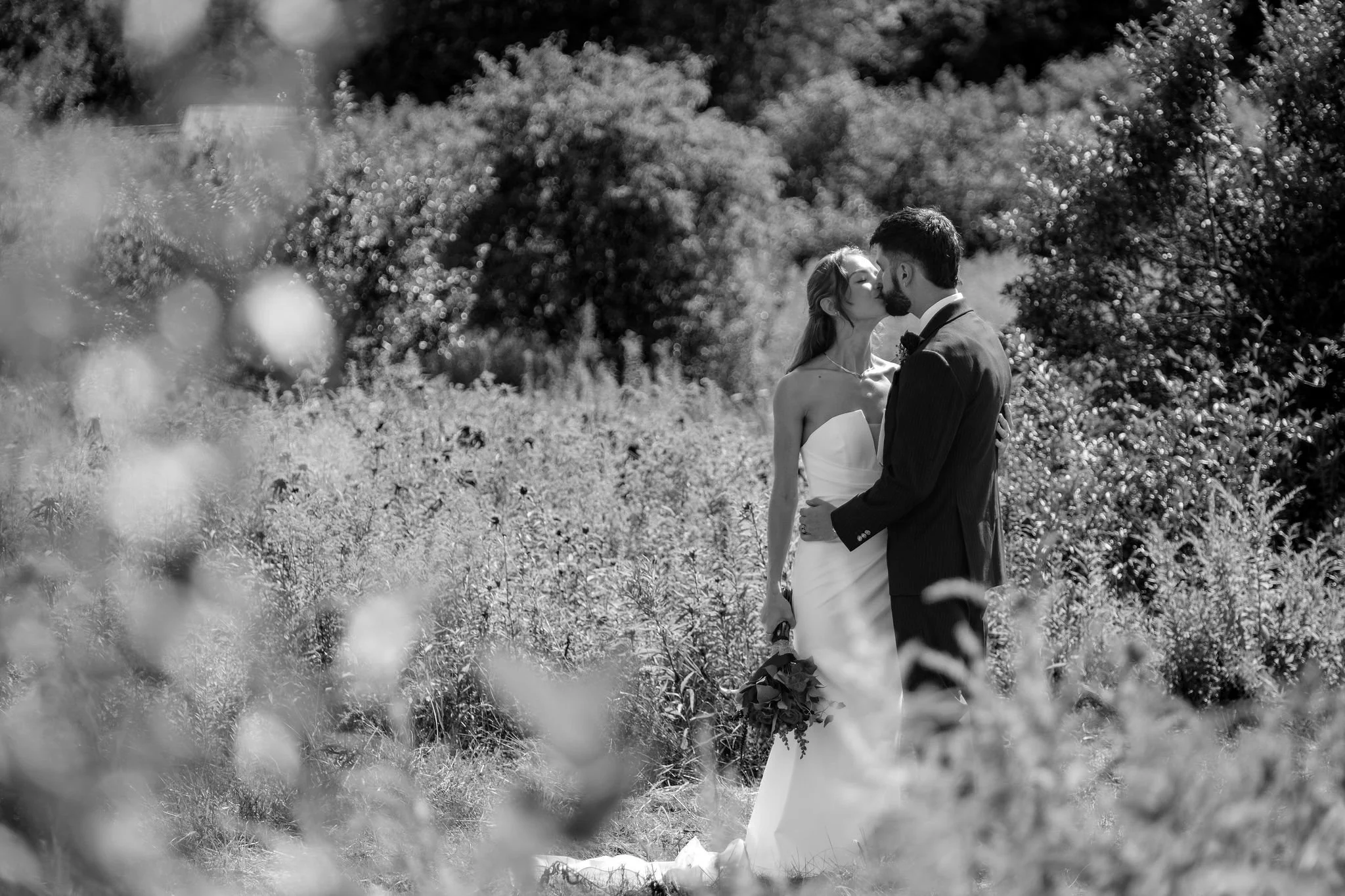 Cassidy and Chase Begin embracing in a wildflower field in black and white at Maple Hill Farm Inn and Conference Center in Hallowell Maine summer wedding photography VMG Productions