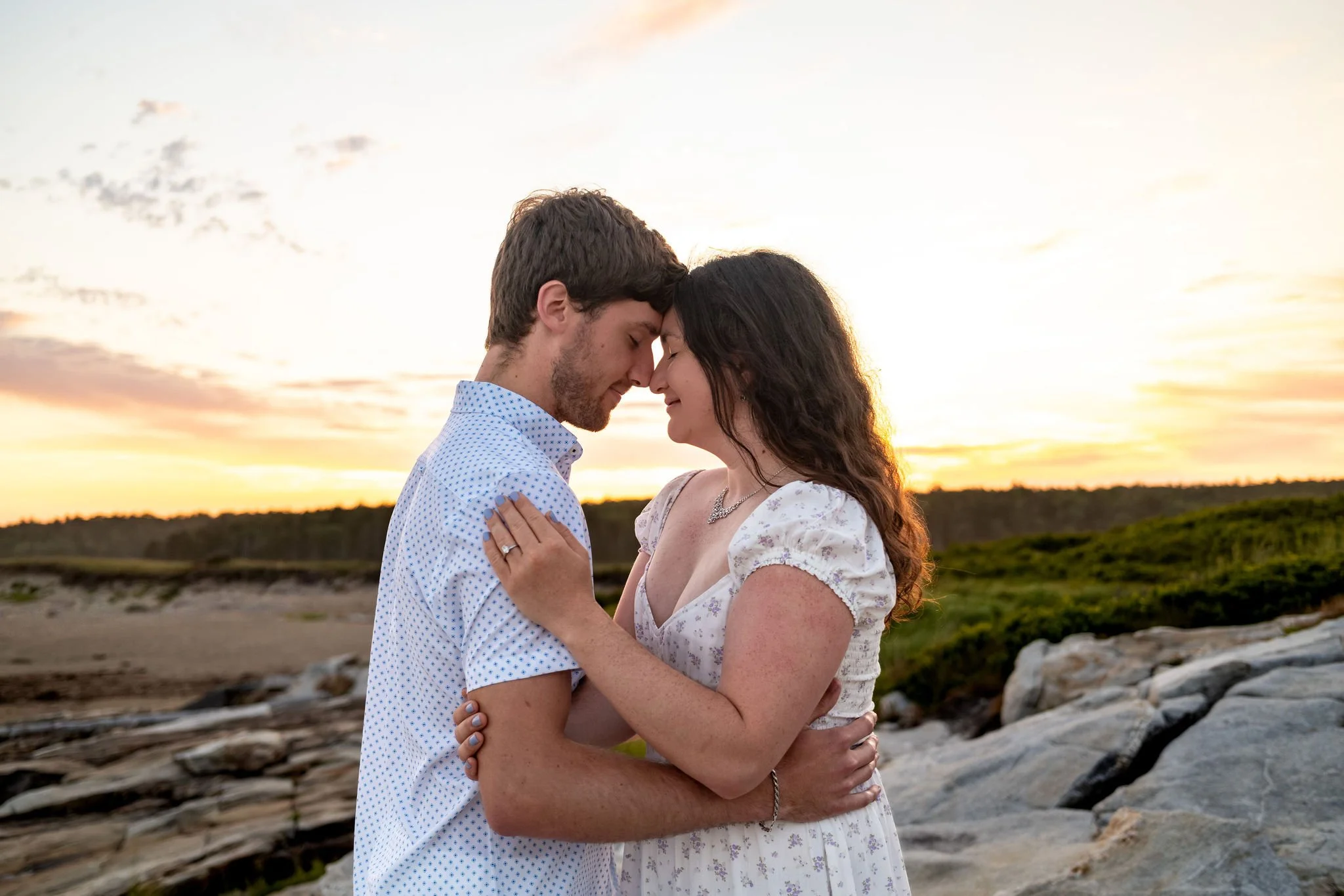 Kirstie and Lucas with their foreheads together on the rocks as the sky fades at Reid State Park in Georgetown Maine engagement photography VMG Productions