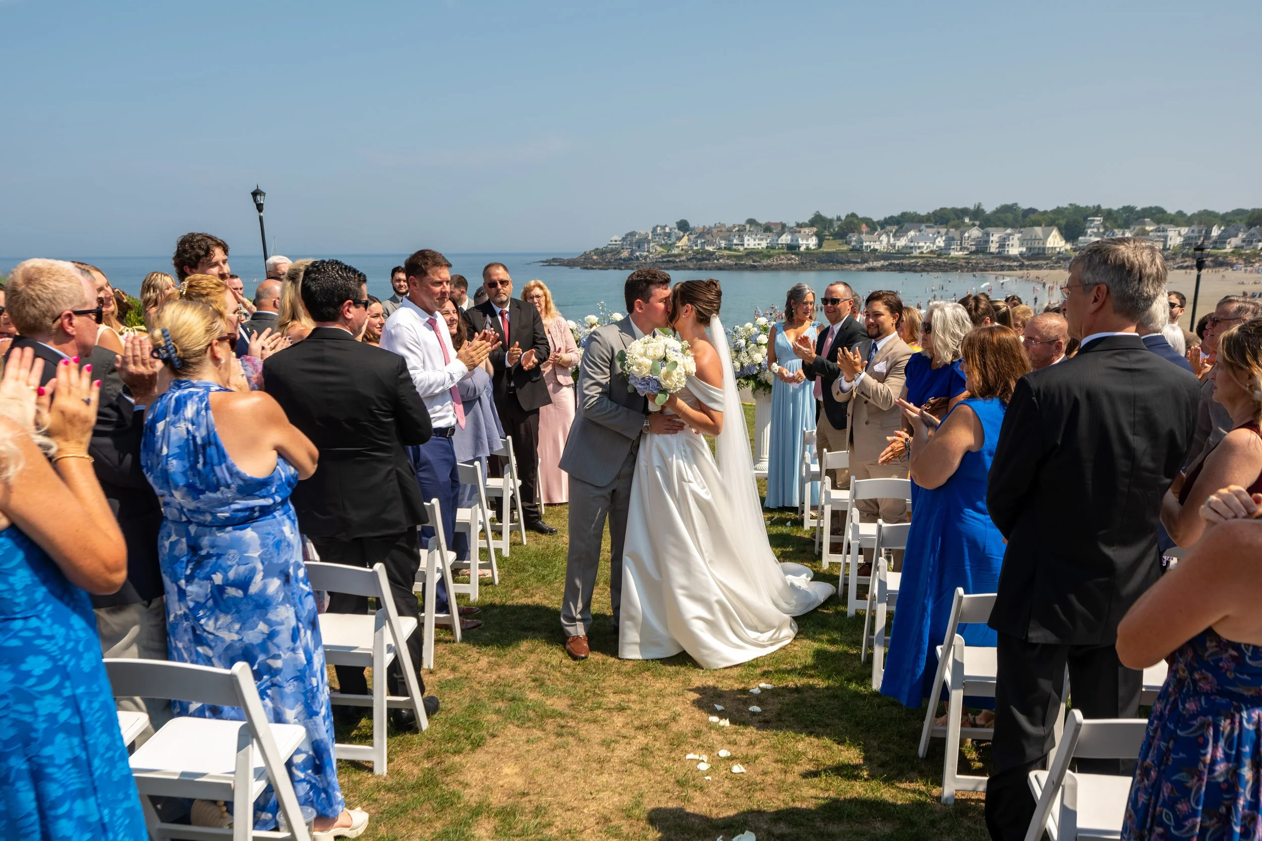 Caroline and Anthony Pirolli kissing during the recessional on the oceanfront lawn with the full York Beach coastline behind them at Union Bluff Hotel wedding photography VMG Productions