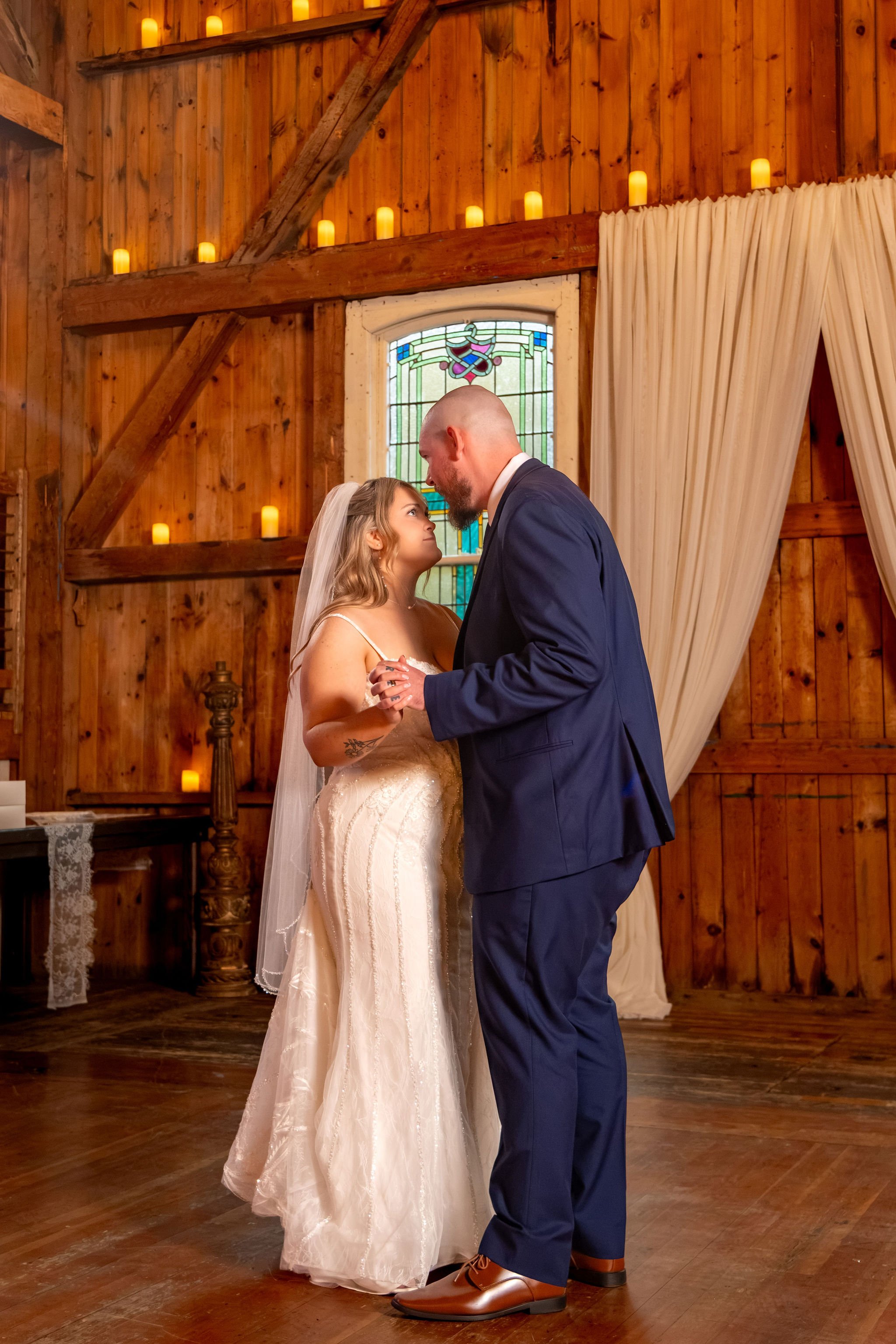 Ellie and Sam sharing a kiss during their first dance under the barn's candlelit walls at Boothbay Playhouse in Boothbay Maine fall wedding photography VMG Productions