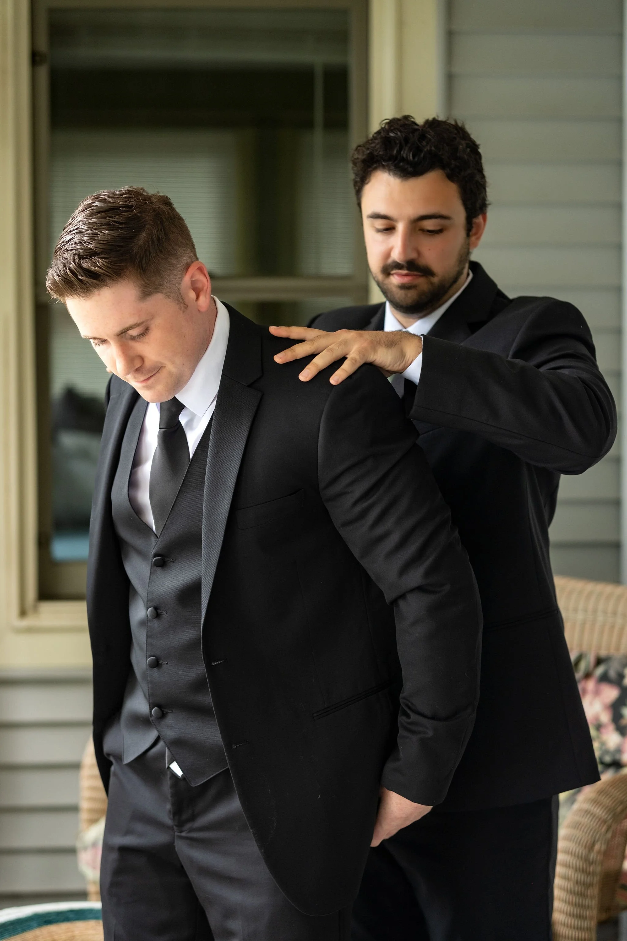 Ethan DeAngelis having his suit jacket adjusted by his best man on the lake house porch in Belmont New Hampshire summer wedding photography VMG Productions