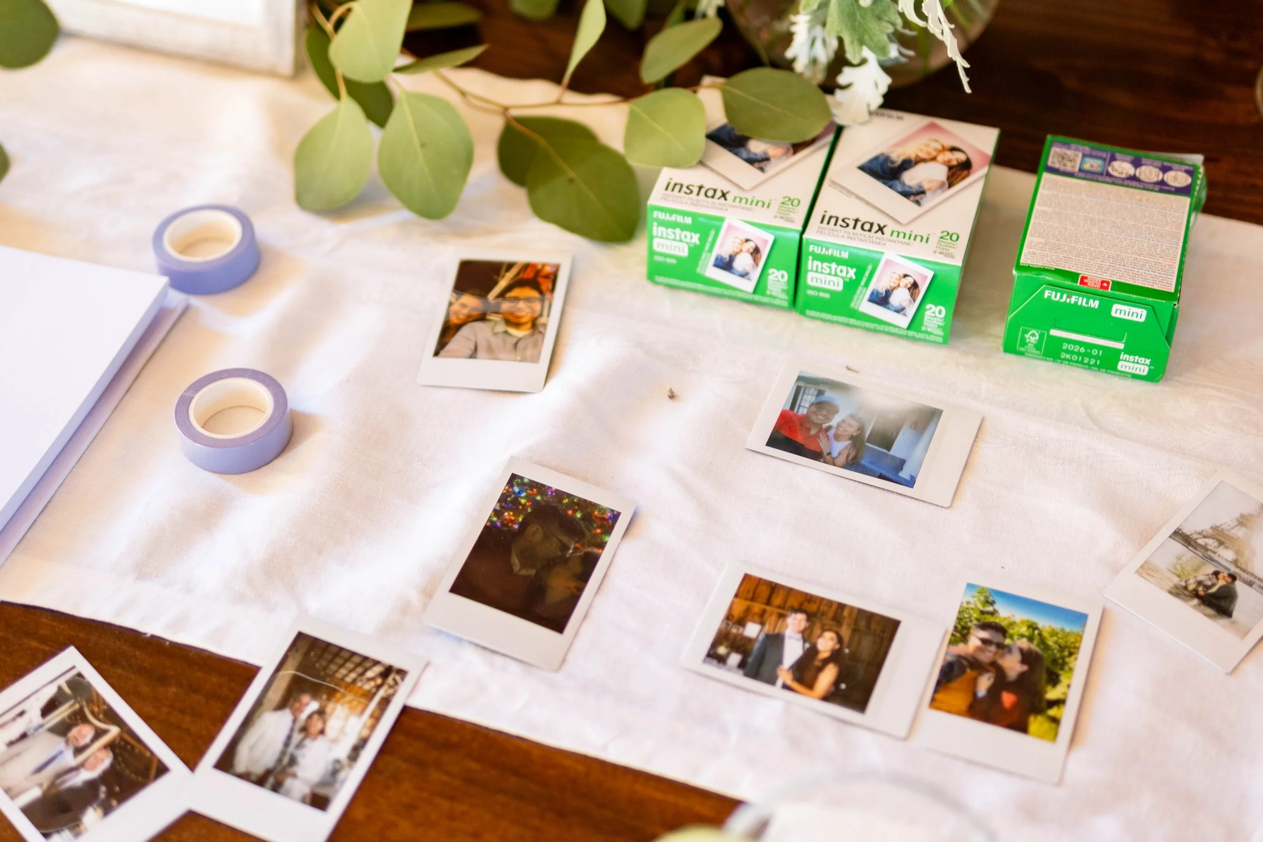 Fujifilm Instax mini film prints spread on linen tablecloth alongside Instax mini film boxes and washi tape at Harmony Hill Farm Warren Maine coastal wedding reception guest book station 2024