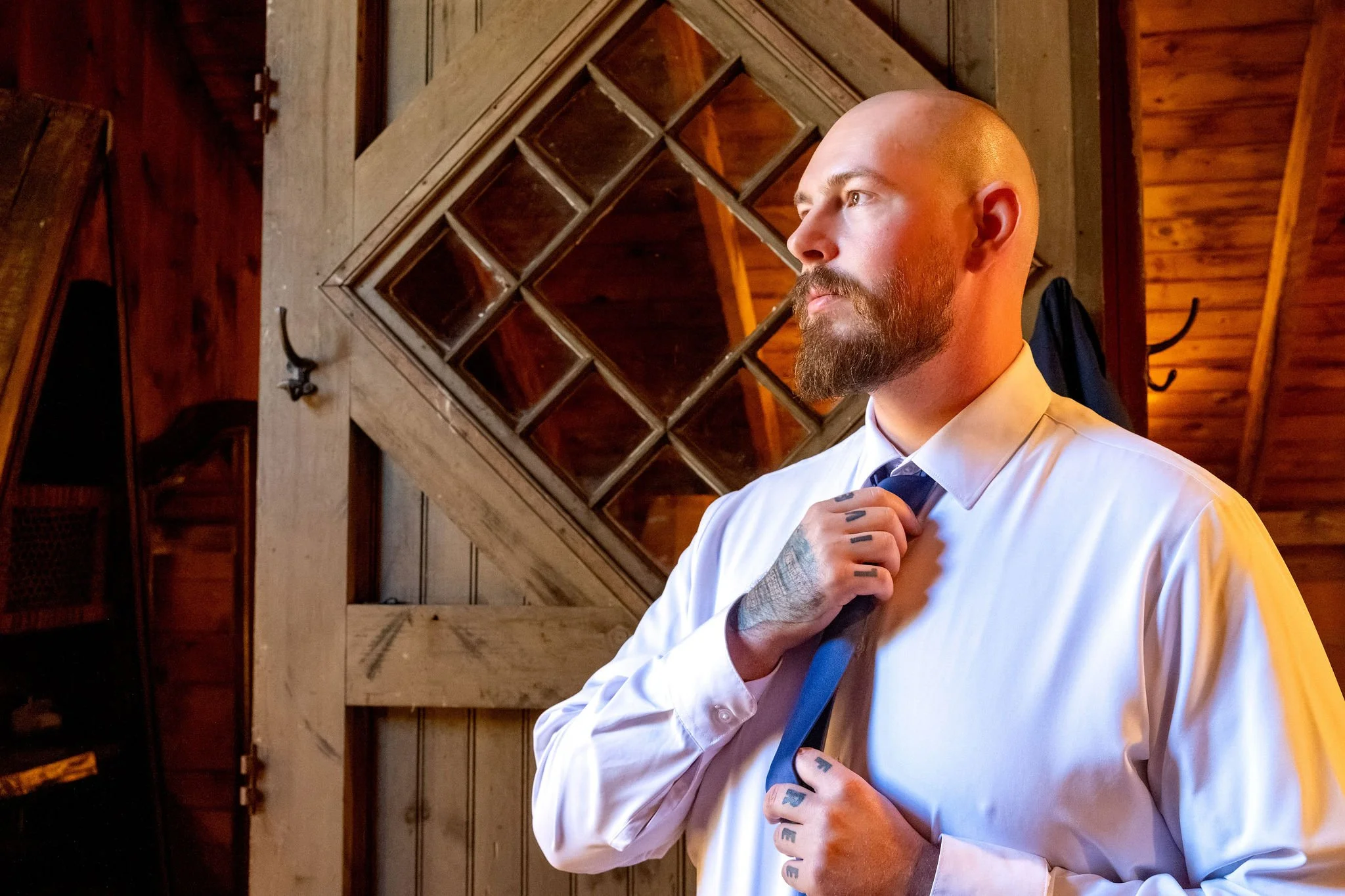 Sam adjusting his blue tie beside a diamond paned barn door at Boothbay Playhouse in Boothbay Maine fall wedding photography VMG Productions
