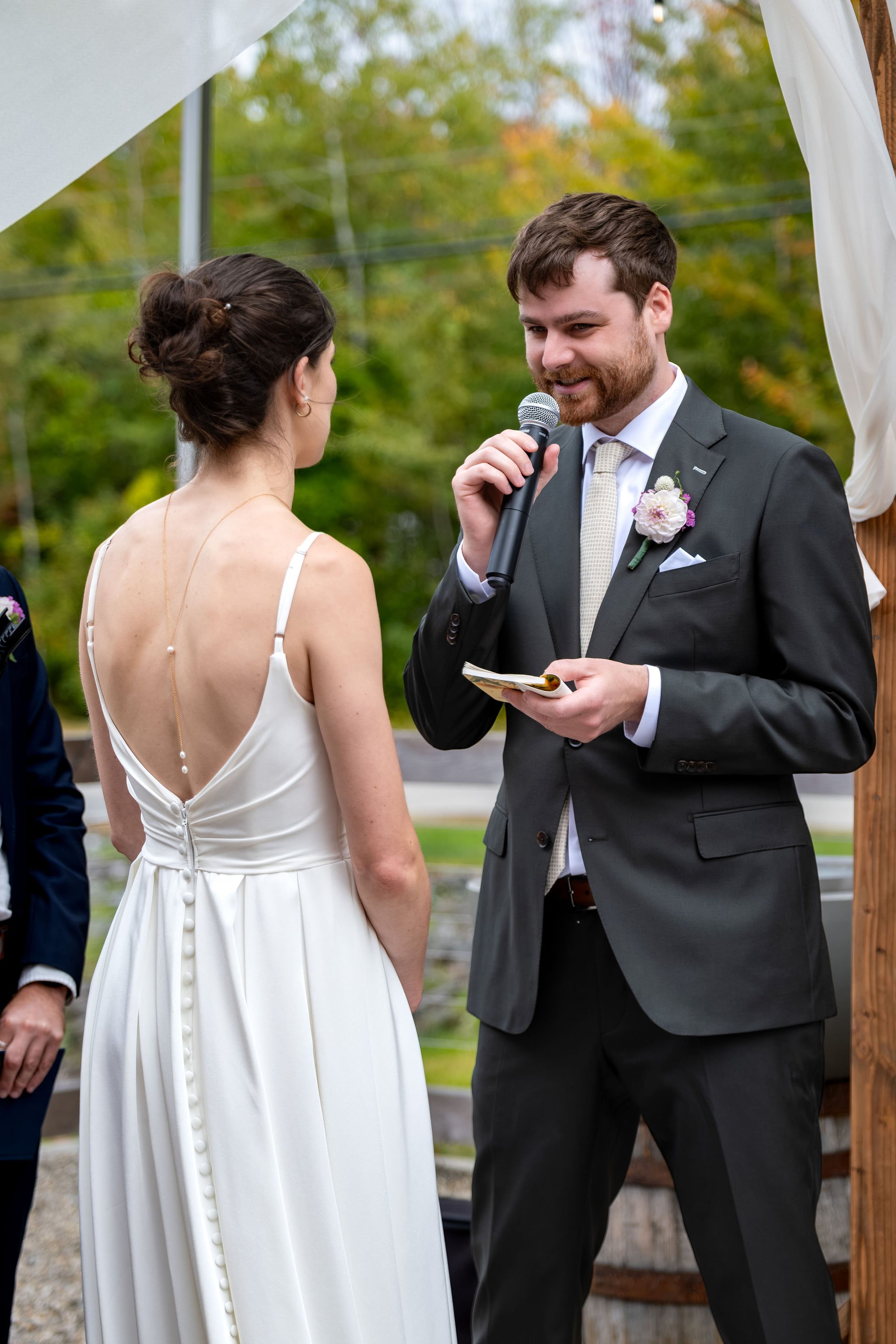 Jack reading his vows into a microphone from a small card at The Cellars at Allagash Brewing Company in Portland Maine fall wedding photography VMG Productions