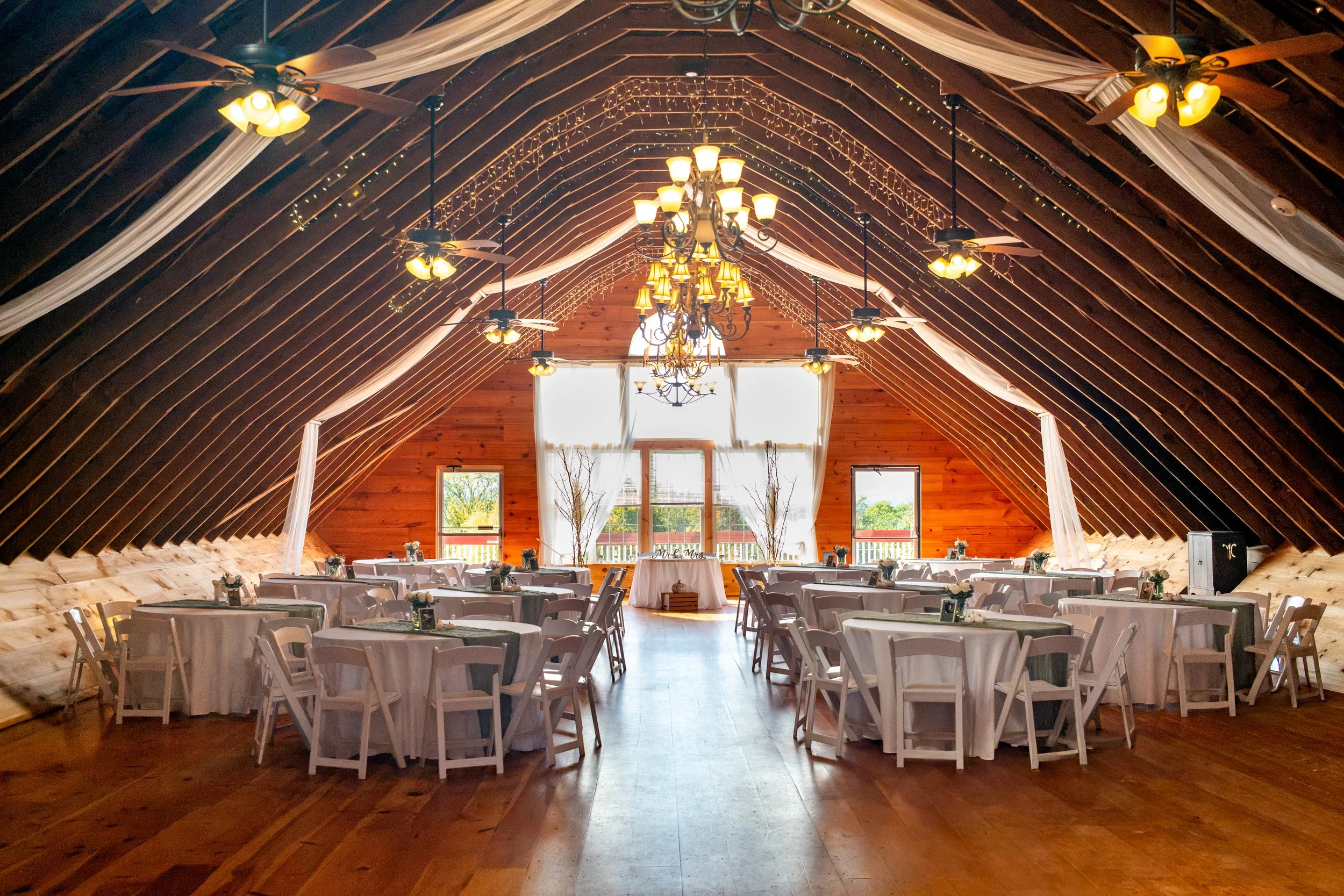 Wide view of the barn reception space with rustic beams, chandeliers, and tables set for dinner at the Maine Wedding Barn and Event Center in Minot Maine fall wedding photography VMG Productions