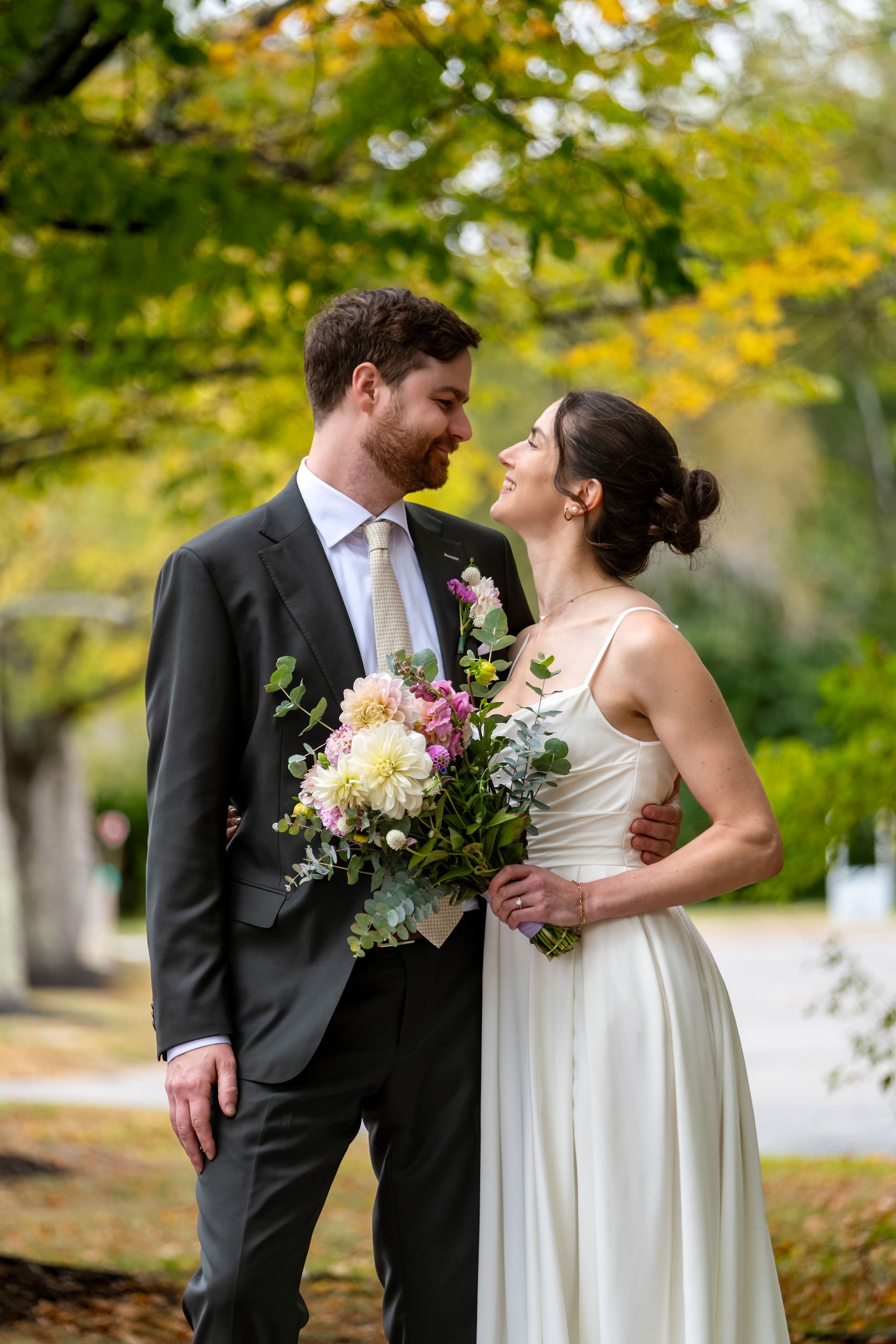 Victoria laughing up at Jack as he holds her close with the bouquet between them at The Cellars at Allagash Brewing Company in Portland Maine fall wedding photography VMG Productions
