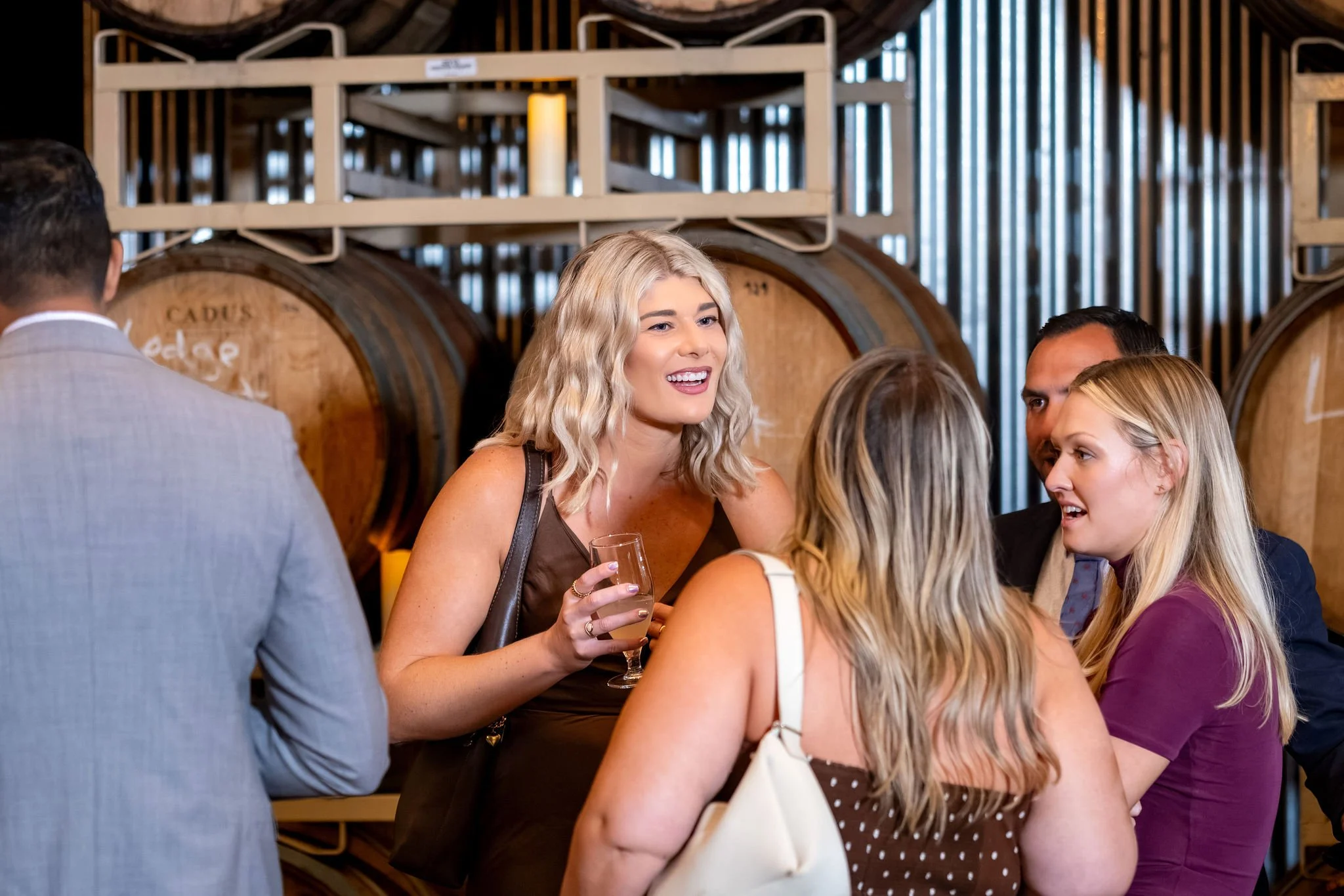 Guests laughing with drinks in hand between the barrel racks at The Cellars at Allagash Brewing Company in Portland Maine fall wedding photography VMG Productions