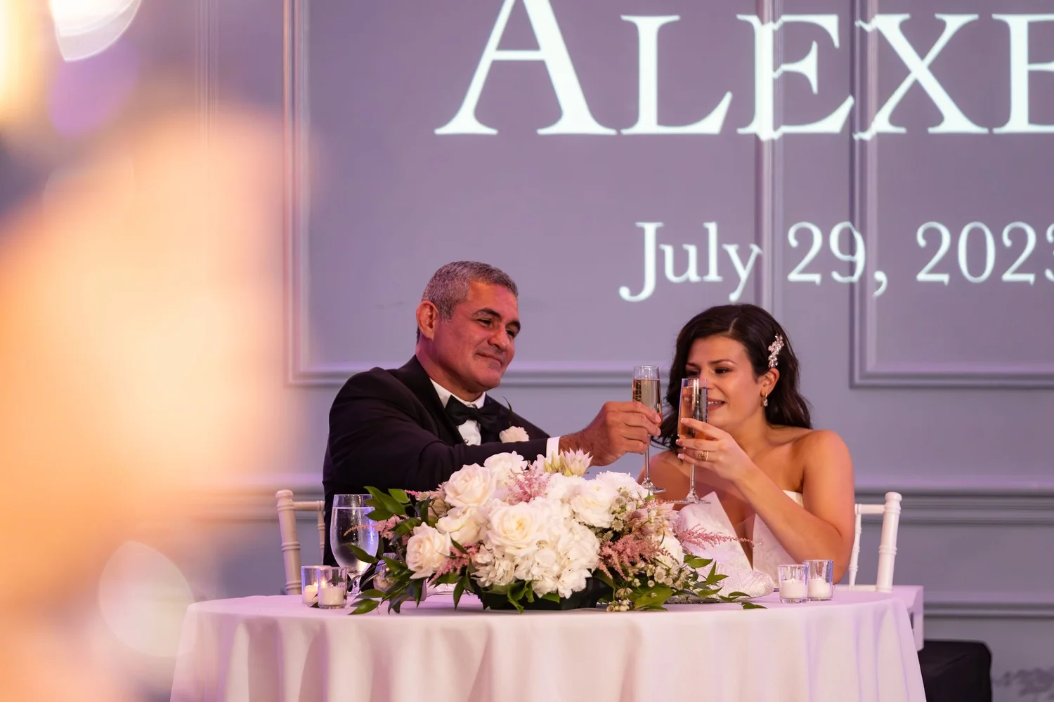 Nicole and Alexey toasting with champagne at their sweetheart table at Portland Sheraton at Sable Oaks South Portland Maine summer wedding photography VMG Productions