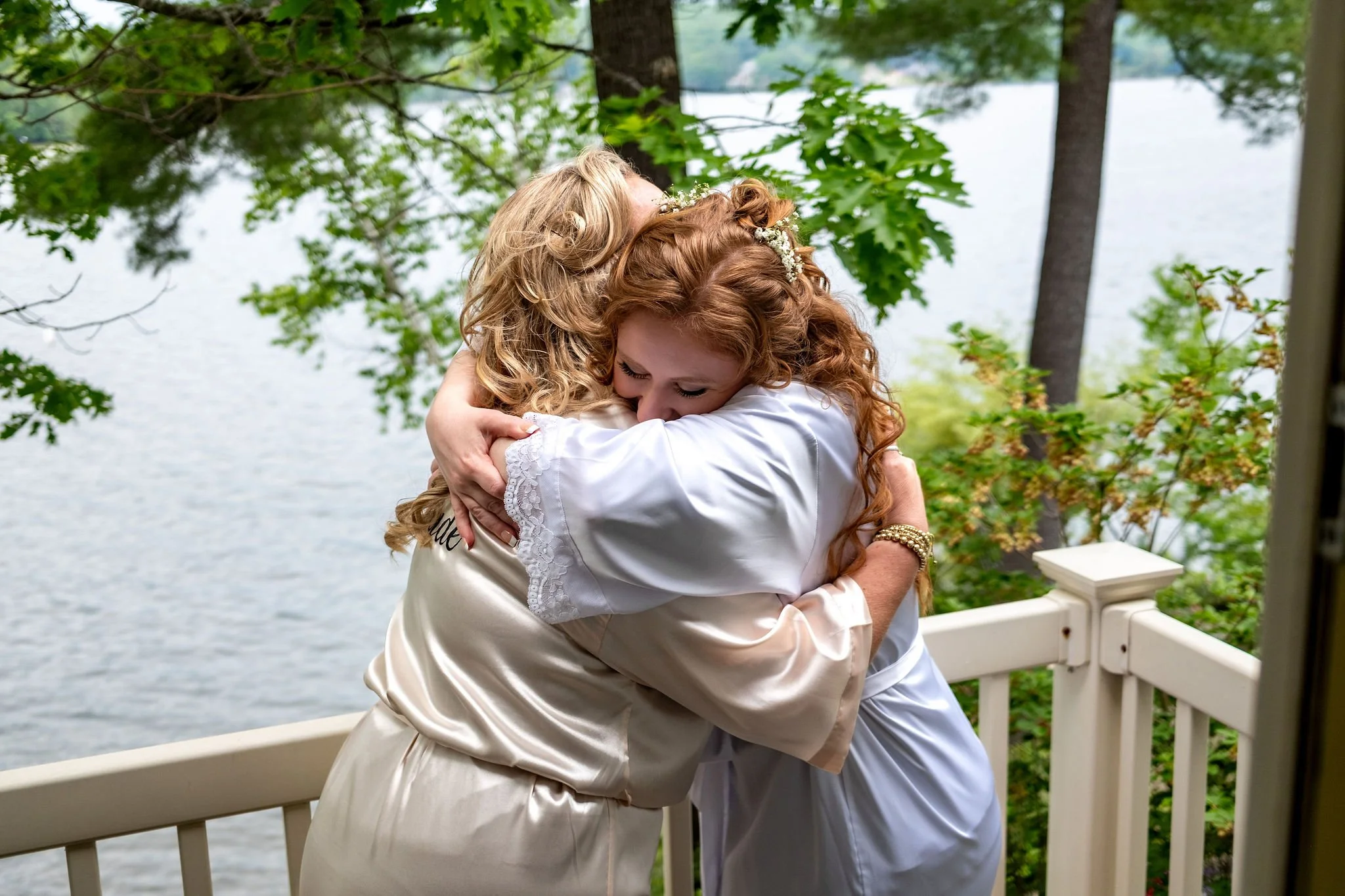 Kayla DeAngelis embracing her maid of honor on the deck overlooking Lake Winnisquam in Belmont New Hampshire summer wedding photography VMG Productions