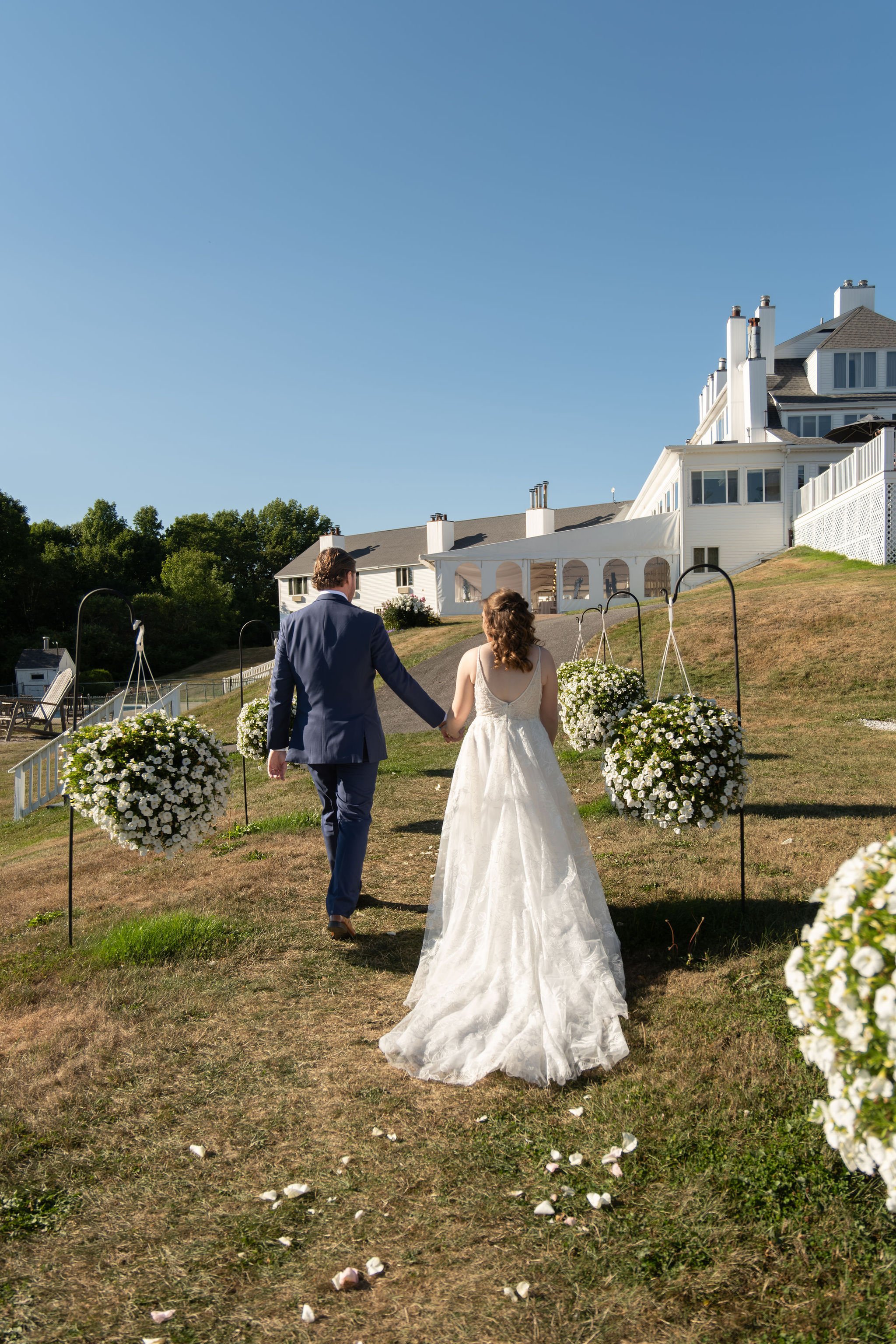 Zachary and Hollie holding hands and walking back up the hillside aisle after the ceremony at The Lucerne Inn in Dedham Maine summer wedding photography VMG Productions