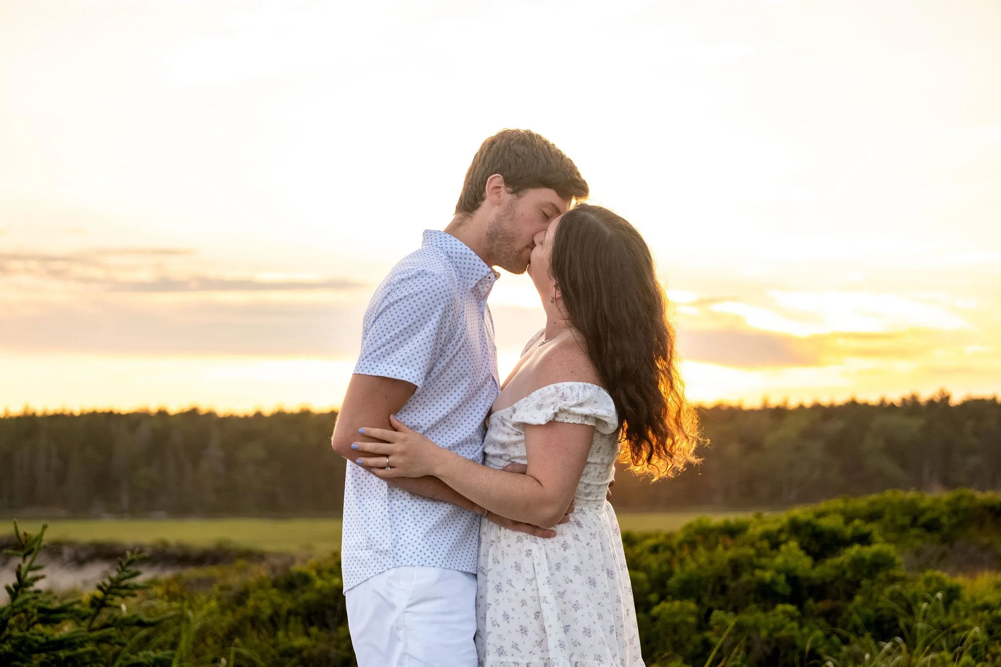 Kirstie and Lucas kissing with the sunset flaring behind them over the marsh at Reid State Park in Georgetown Maine engagement photography VMG Productions