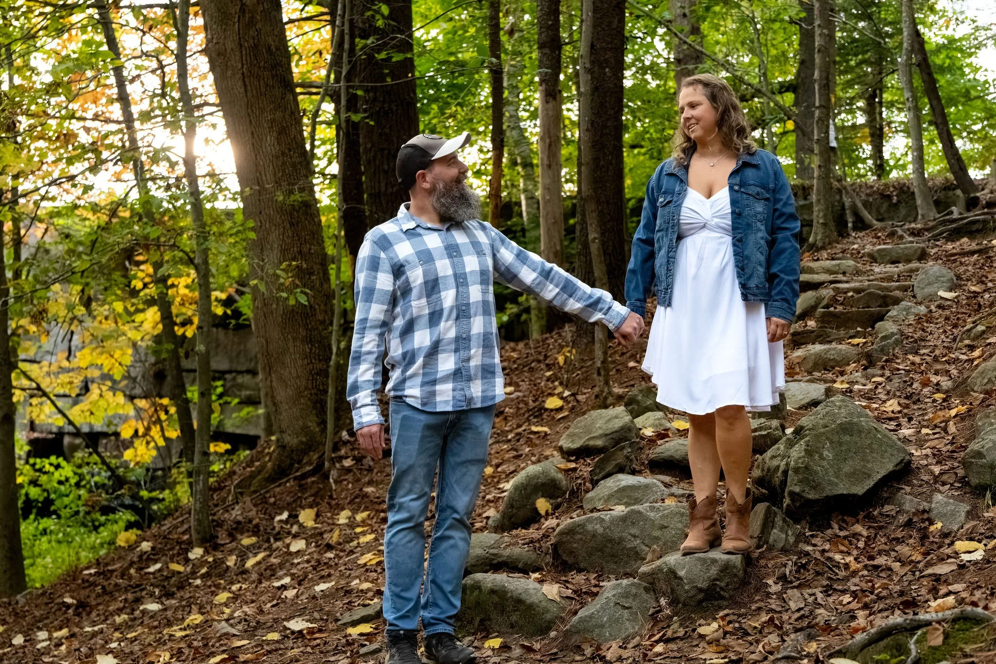 Dave leading Alison by the hand down the old stone stairs through the woods with yellow leaves overhead at Vaughan Woods in Hallowell Maine fall engagement photography VMG Productions