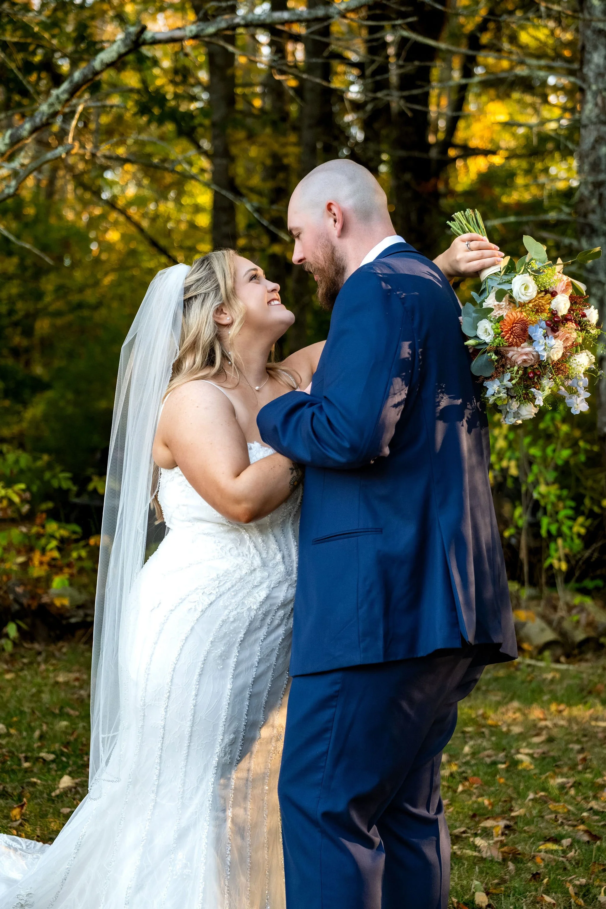 Ellie looking up at Sam with a huge smile in the fall woods at Boothbay Playhouse in Boothbay Maine fall wedding photography VMG Productions