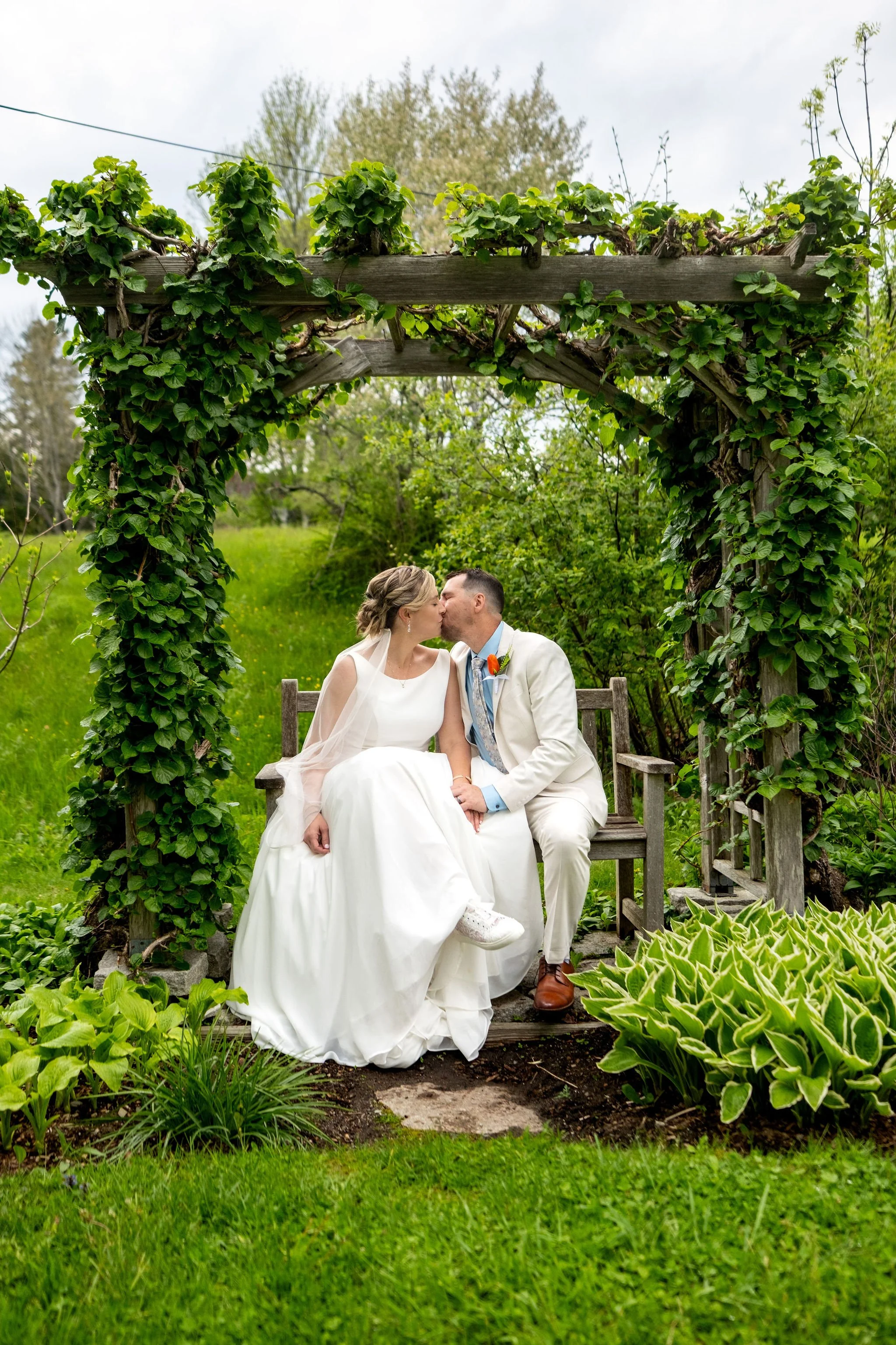Alli and Adam Baudoin kissing beneath the garden arbor in Somesville Maine spring wedding photography VMG Productions