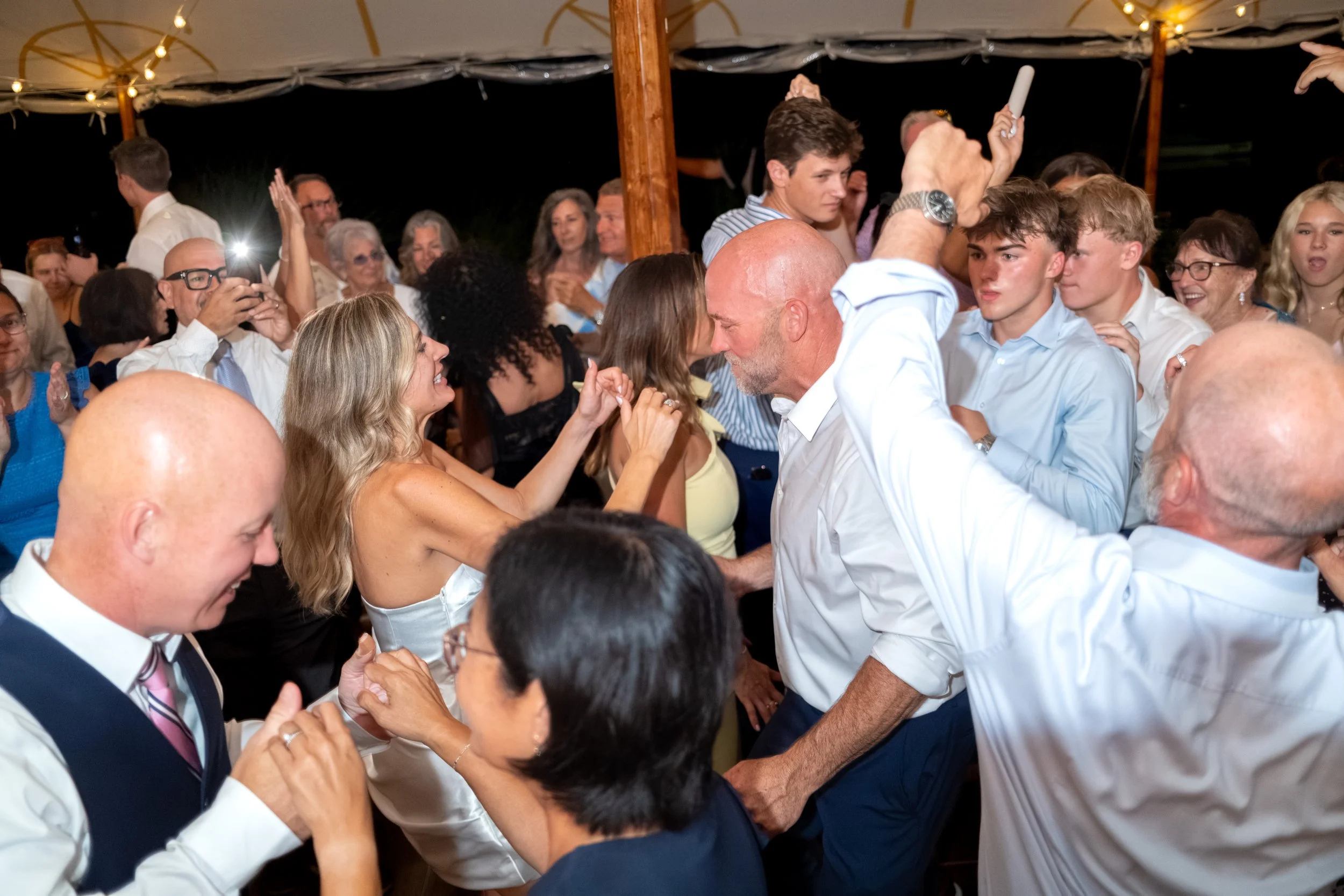 Ashley and Marc Draper lifted above the crowd with hands clasped at the height of the party at The Breakwater Inn in Kennebunkport Maine summer wedding photography VMG Productions