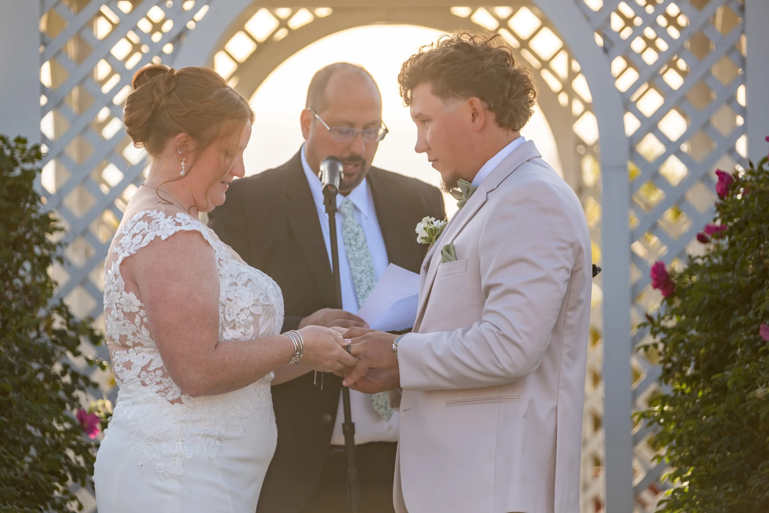 Erika and Andrew exchanging rings in front of the officiant under the white lattice gazebo at the Maine Wedding Barn and Event Center in Minot Maine fall wedding photography VMG Productions