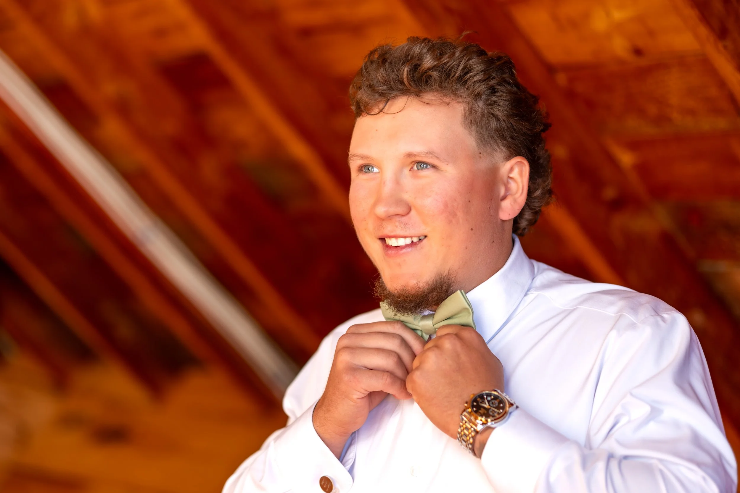 Andrew adjusting his bow tie in front of the barn's warm wood walls at the Maine Wedding Barn and Event Center in Minot Maine fall wedding photography VMG Productions