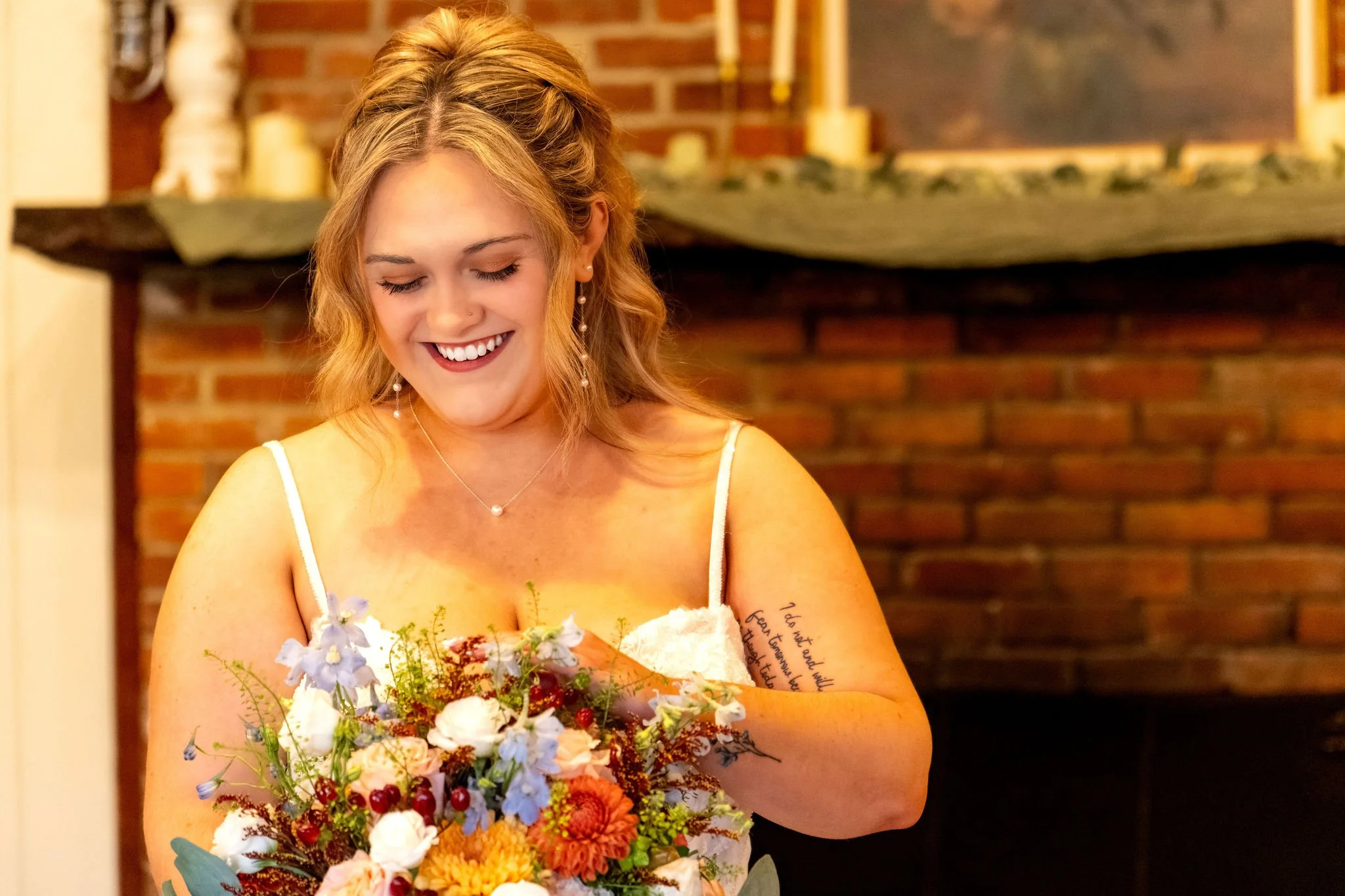 Ellie laughing as she looks down at her burnt orange and dusty blue bouquet at Boothbay Playhouse in Boothbay Maine fall wedding photography VMG Productions
