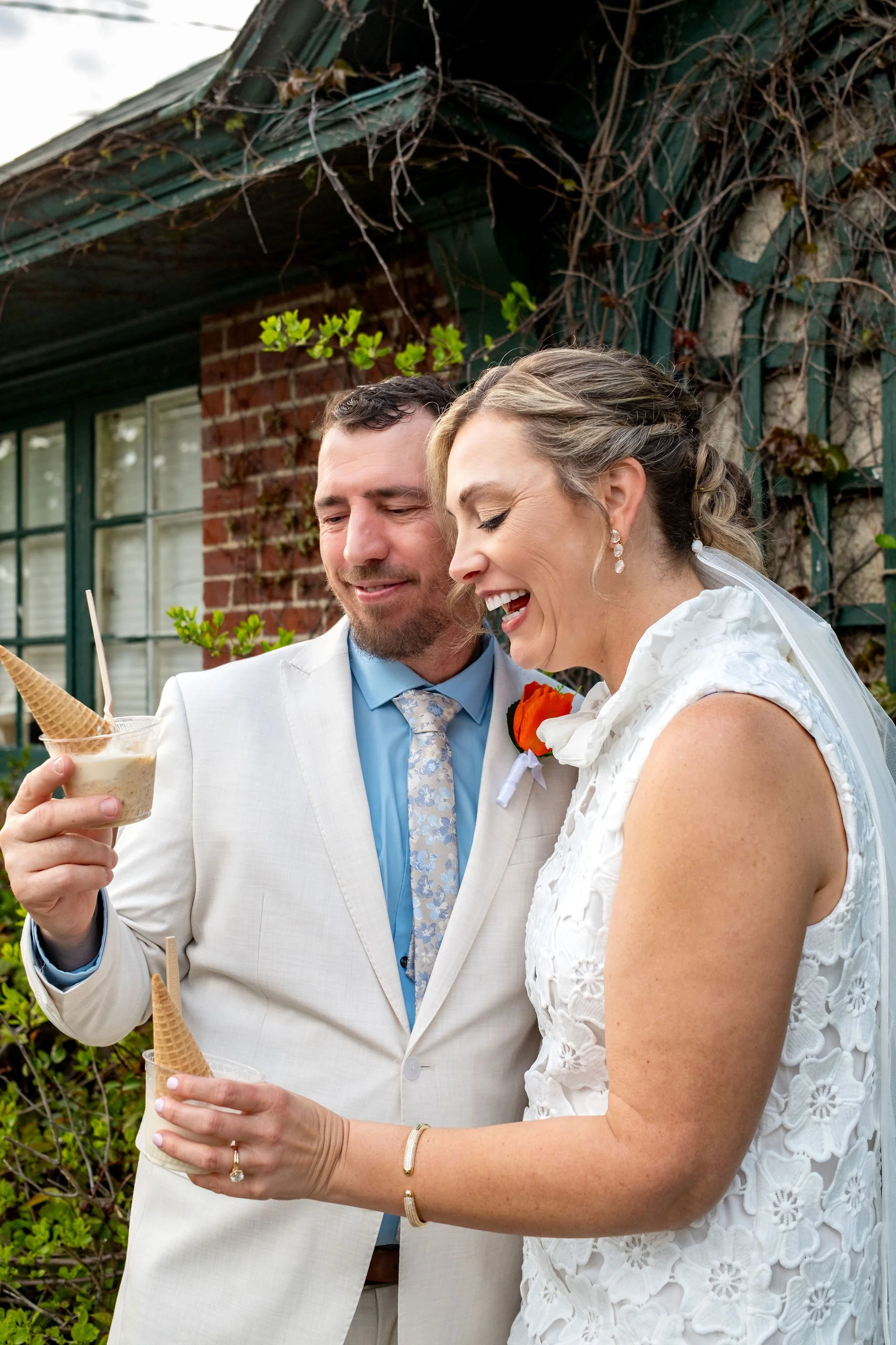 Alli and Adam Baudoin laughing over ice cream cones outside Mount Desert Island Ice Cream in Bar Harbor Maine spring wedding photography VMG Productions