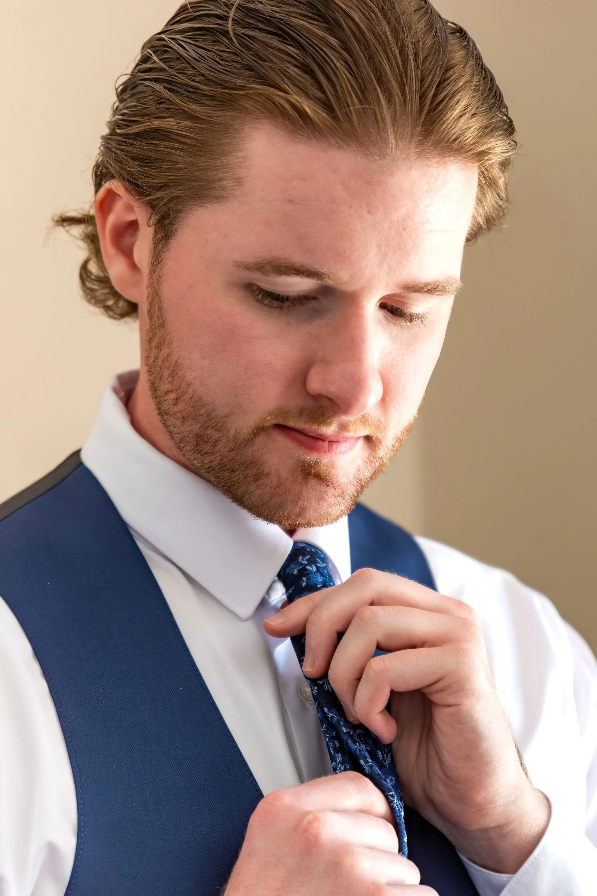 Zachary tightening his navy floral tie in a white shirt and navy vest while getting ready at The Lucerne Inn in Dedham Maine summer wedding photography VMG Productions