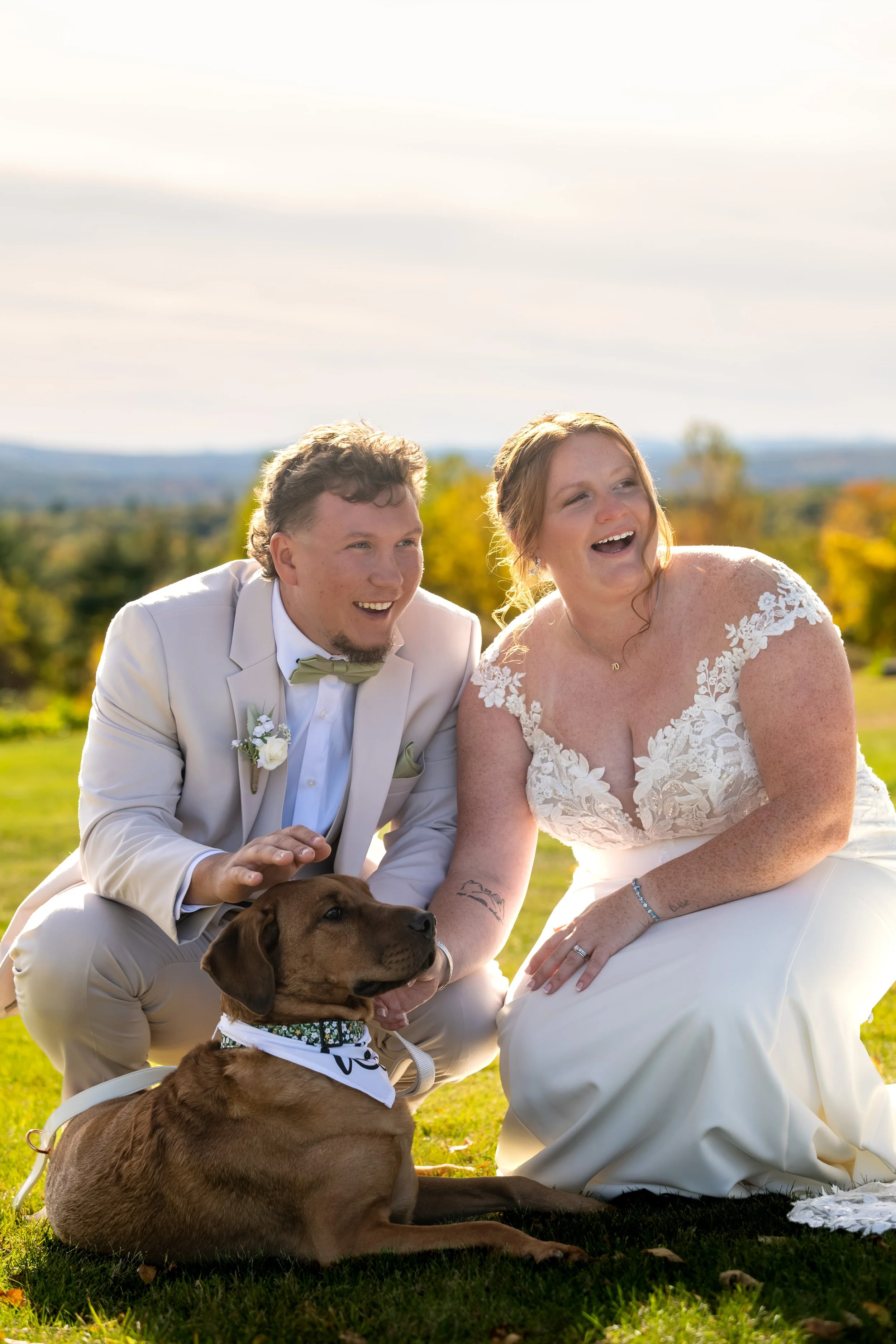 Andrew and Erika laughing as they pet Penny on the lawn at the Maine Wedding Barn and Event Center in Minot Maine fall wedding photography VMG Productions
