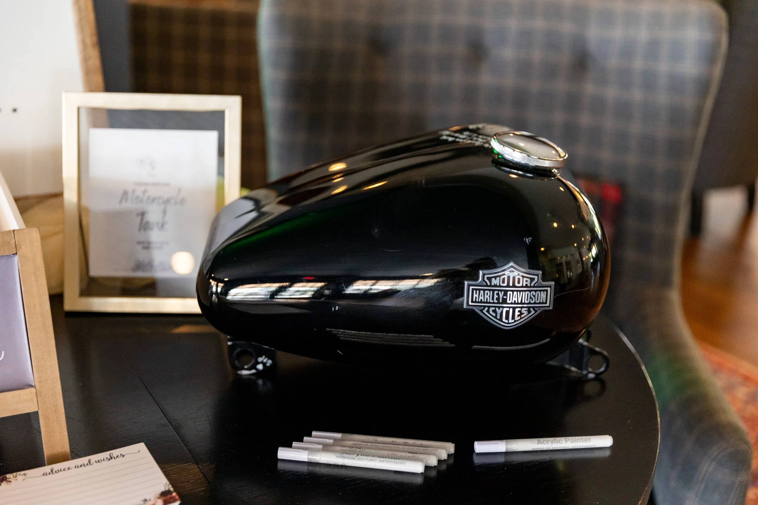Black Harley Davidson motorcycle tank with white acrylic paint markers for wedding guests to sign as guest book at Wentworth Inn Jackson New Hampshire wedding reception 2024