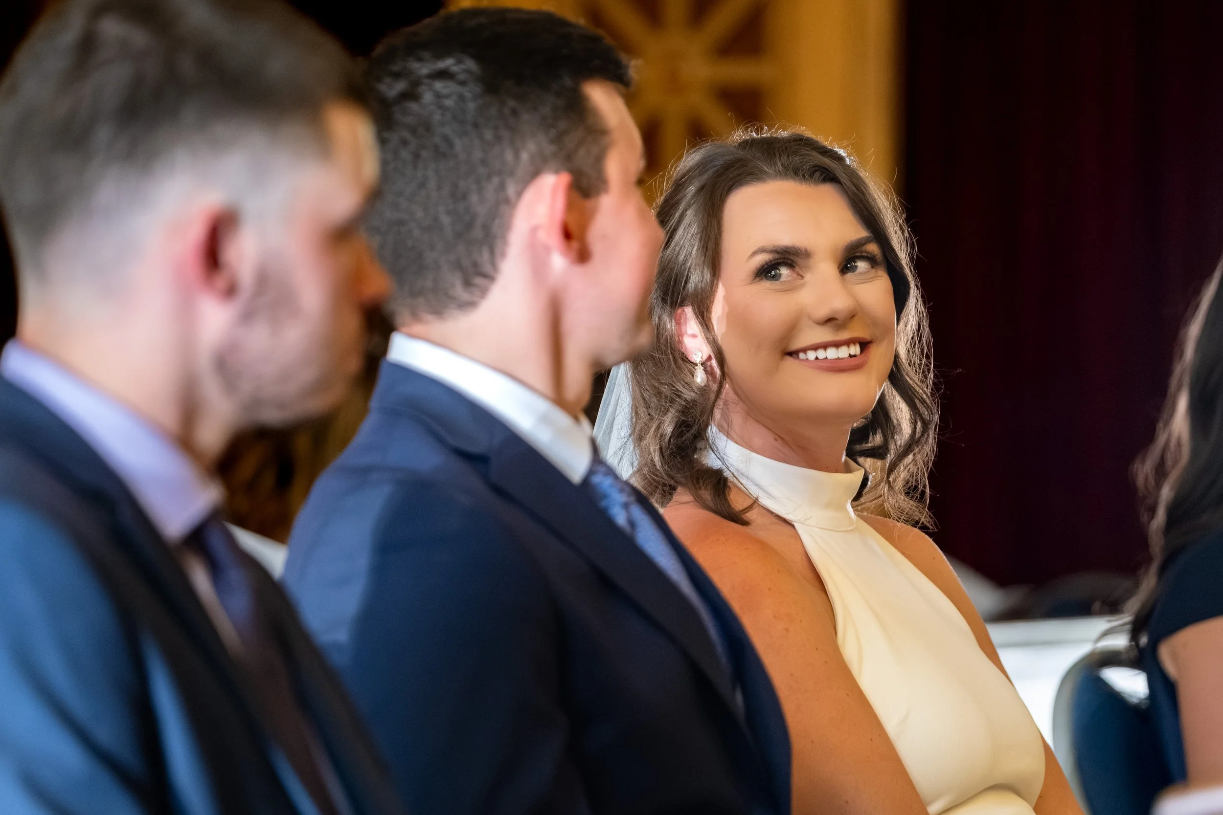 Caroline Pirolli smiling during the Mass through foreground guests at Star of the Sea Catholic Church in York Maine wedding photography VMG Productions