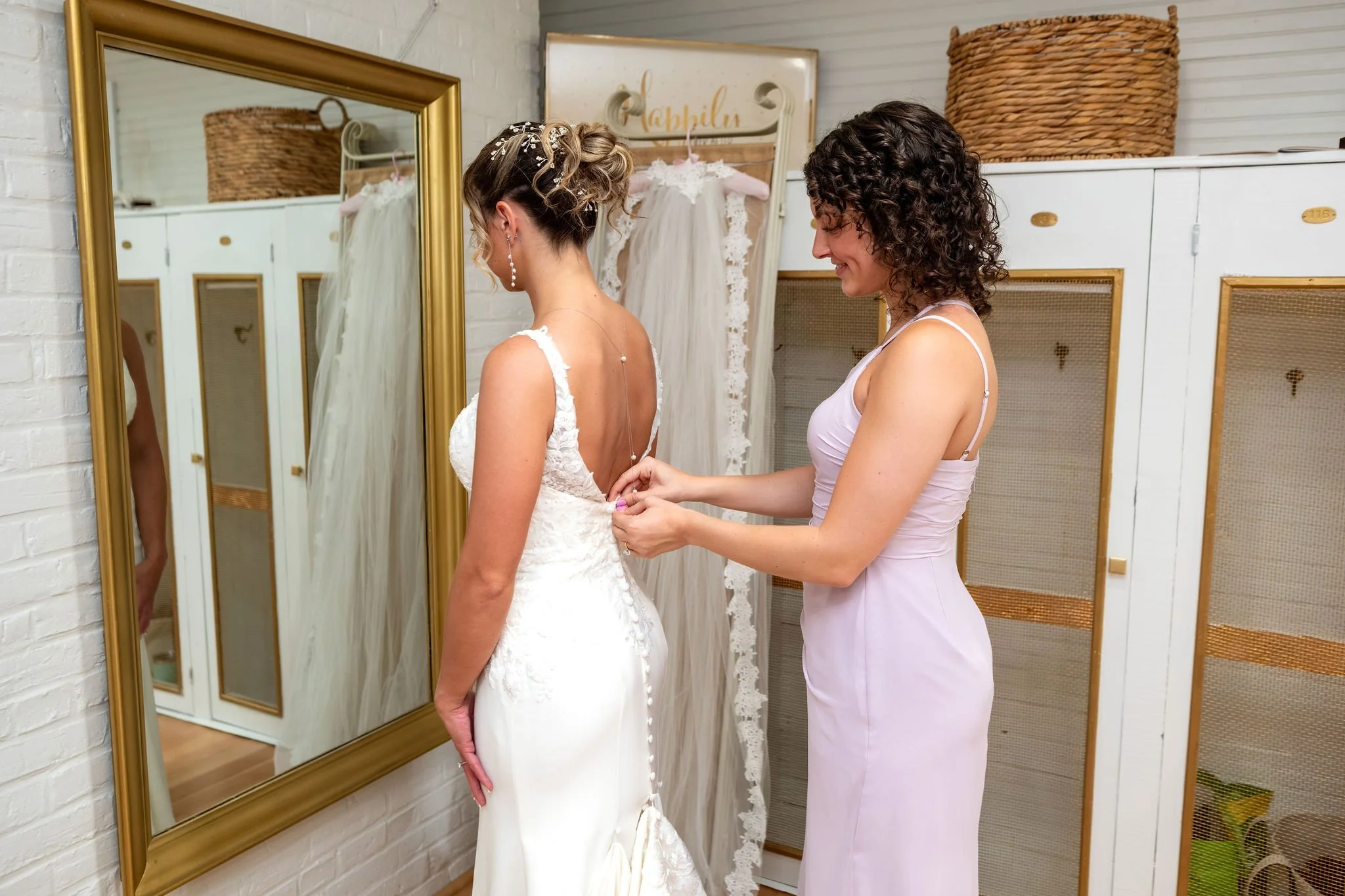 Beth and Cameron a bridesmaid fastening the bride's gown at Augusta Country Club Manchester Maine spring wedding photography VMG Productions