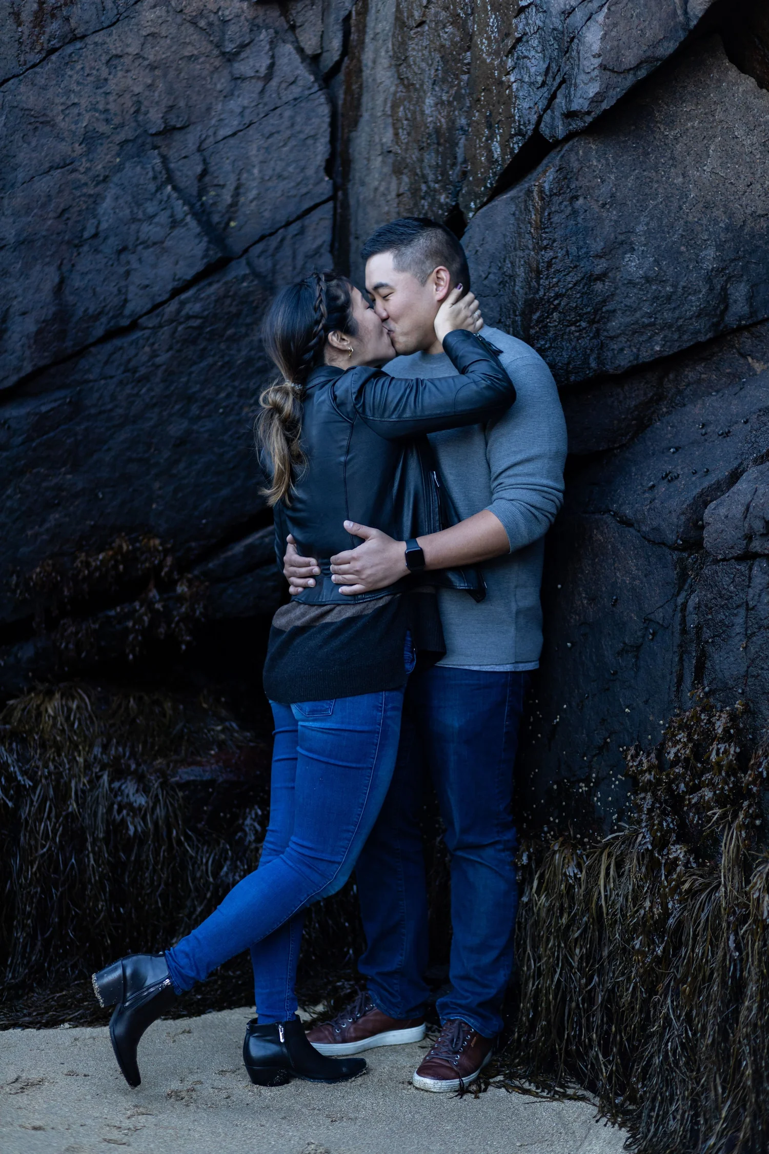 Agnes and Peter kissing against dark granite rock wall coastline Acadia National Park engagement VMG Productions