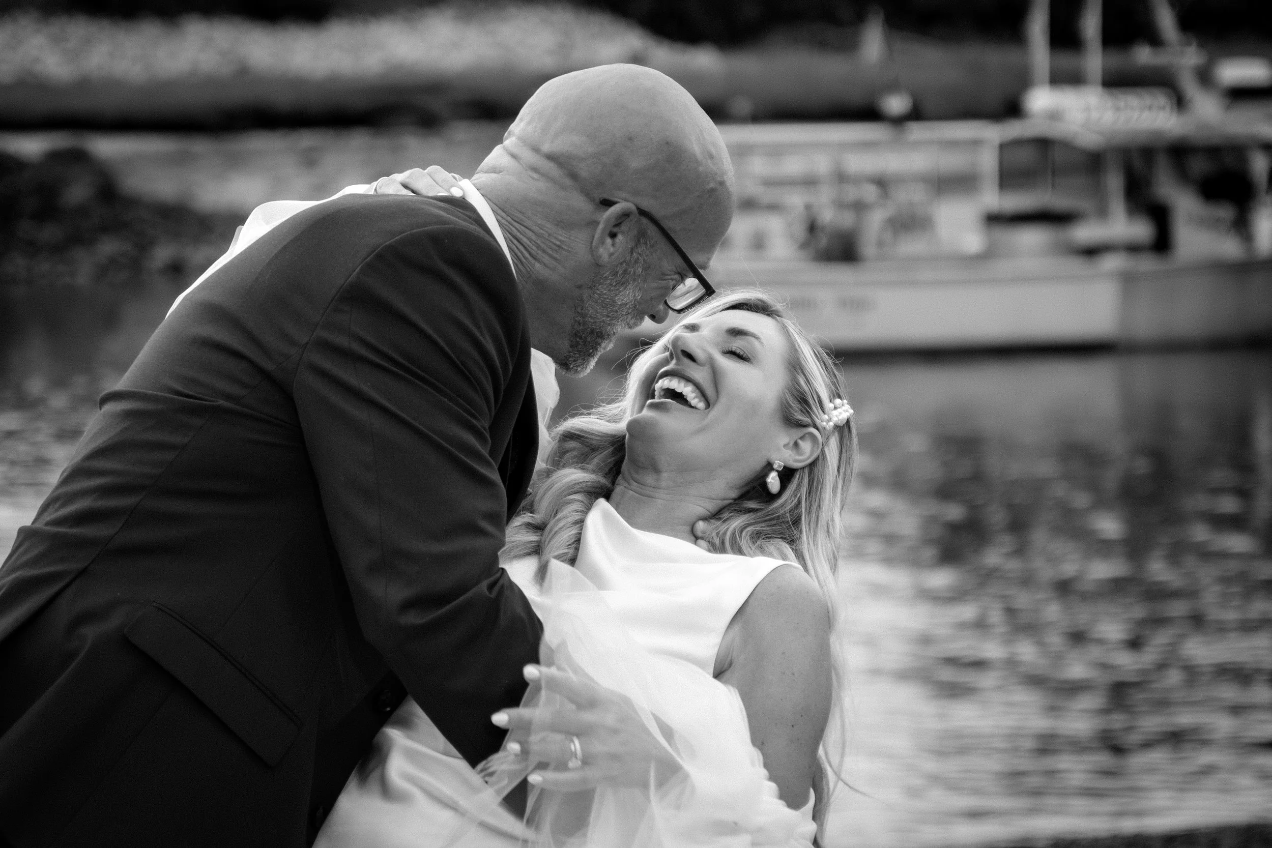 Marc Draper dipping Ashley as she laughs on the shoreline with a lobster boat behind them in black and white at The Breakwater Inn in Kennebunkport Maine summer wedding photography VMG Productions