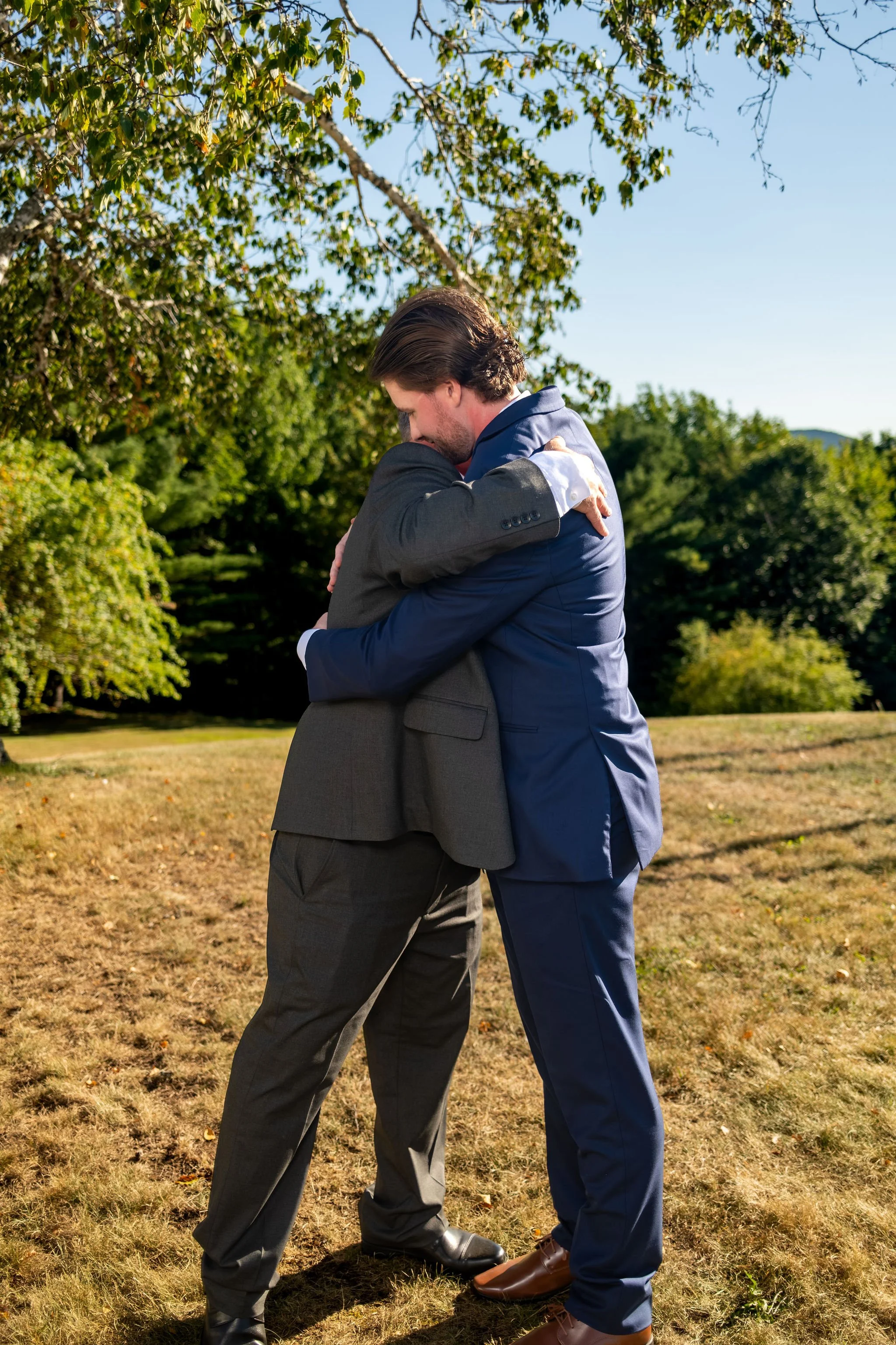 Hollie's dad wrapping Zachary in a long hug under the birch trees after the ceremony at The Lucerne Inn in Dedham Maine summer wedding photography VMG Productions