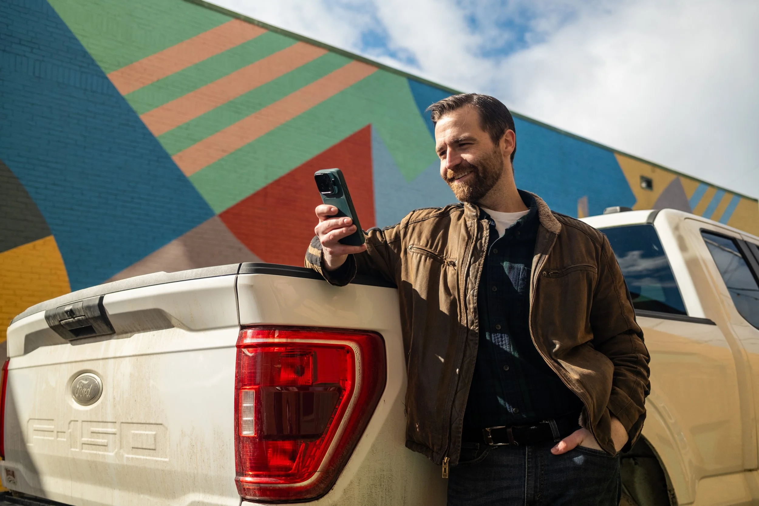Member with phone beside a pickup and mural