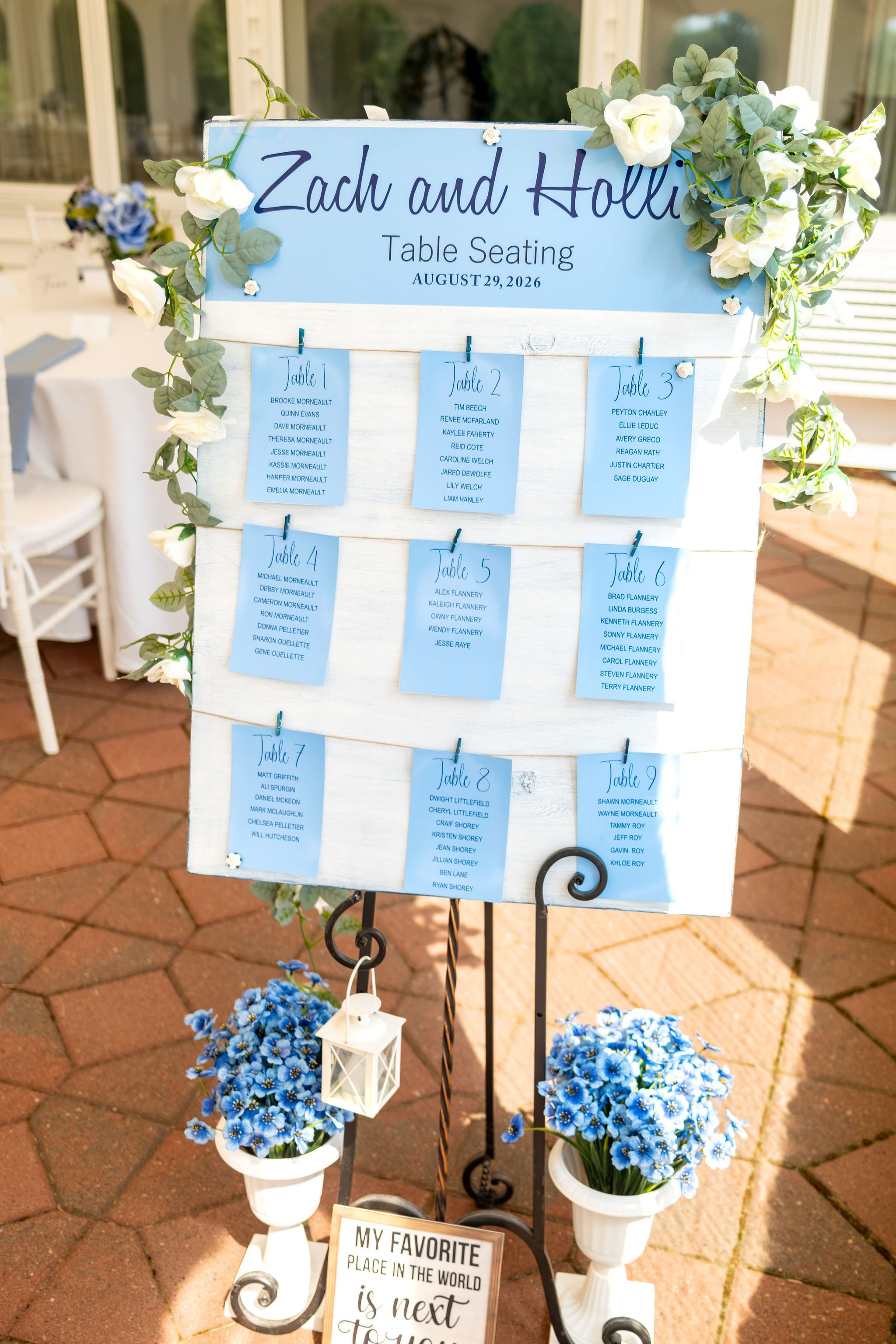 Zachary and Hollie's table seating chart in blue on an easel with white florals under the tent at The Lucerne Inn in Dedham Maine summer wedding photography VMG Productions