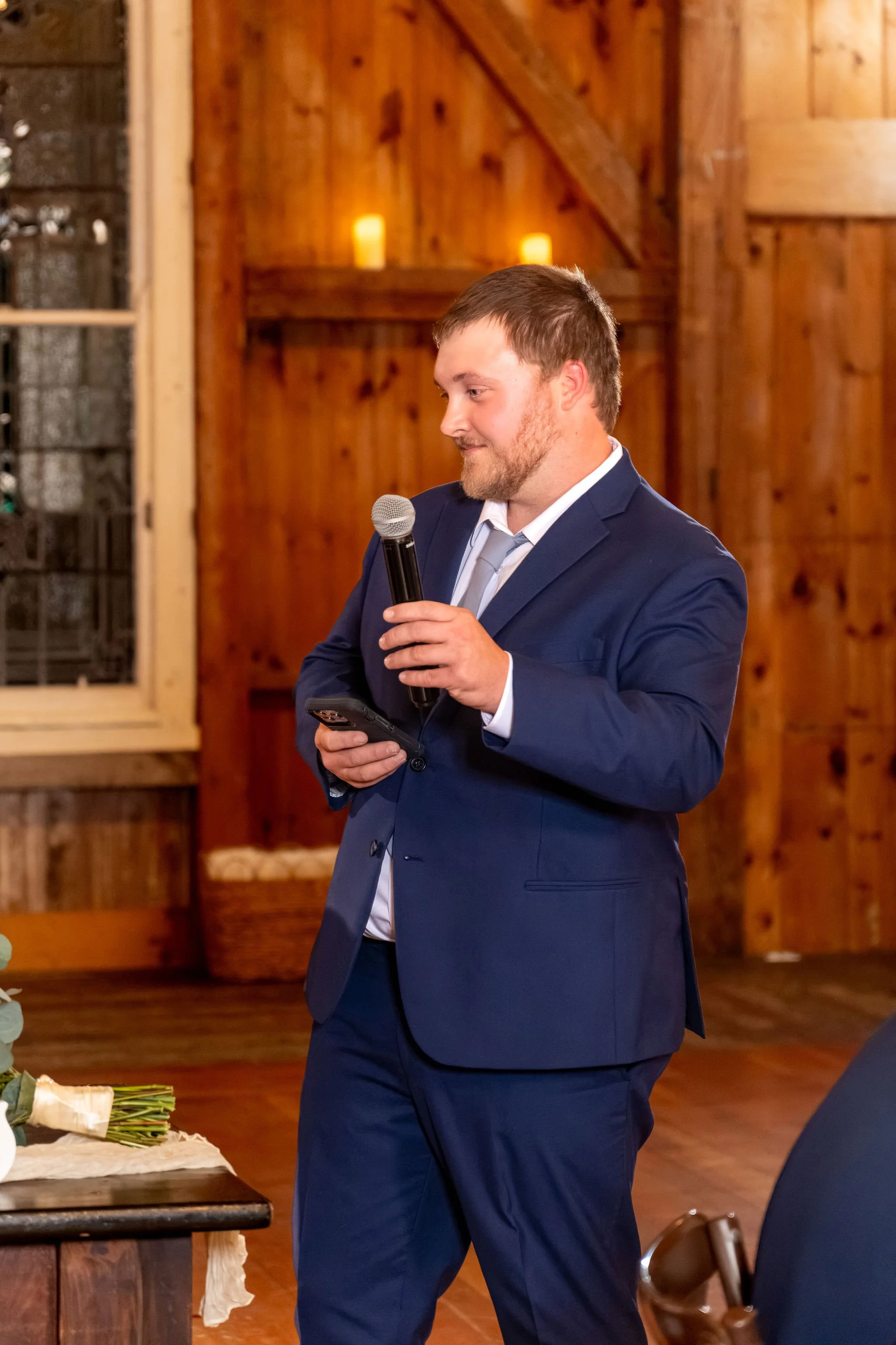 The best man giving his toast into a microphone in the candlelit barn at Boothbay Playhouse in Boothbay Maine fall wedding photography VMG Productions