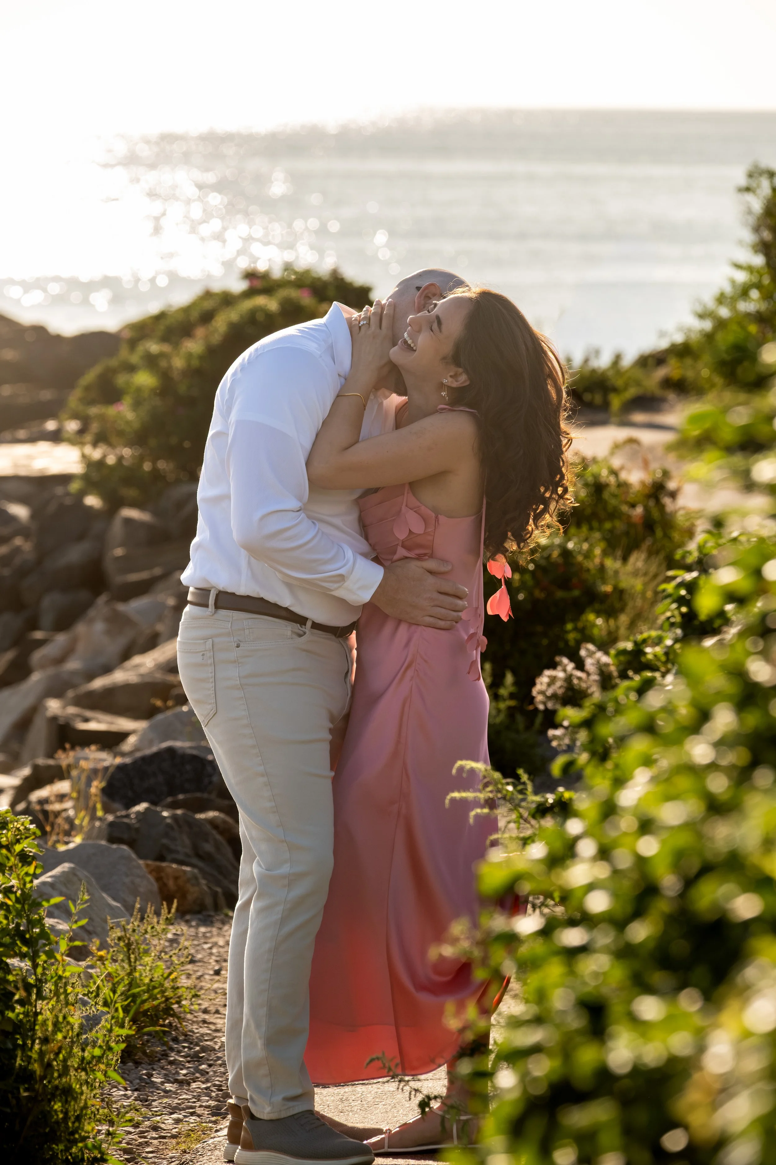 Helena laughing with her head tossed back in Zack's arms on the coastal path on Marginal Way in Ogunquit Maine sunrise proposal and engagement photography VMG Productions