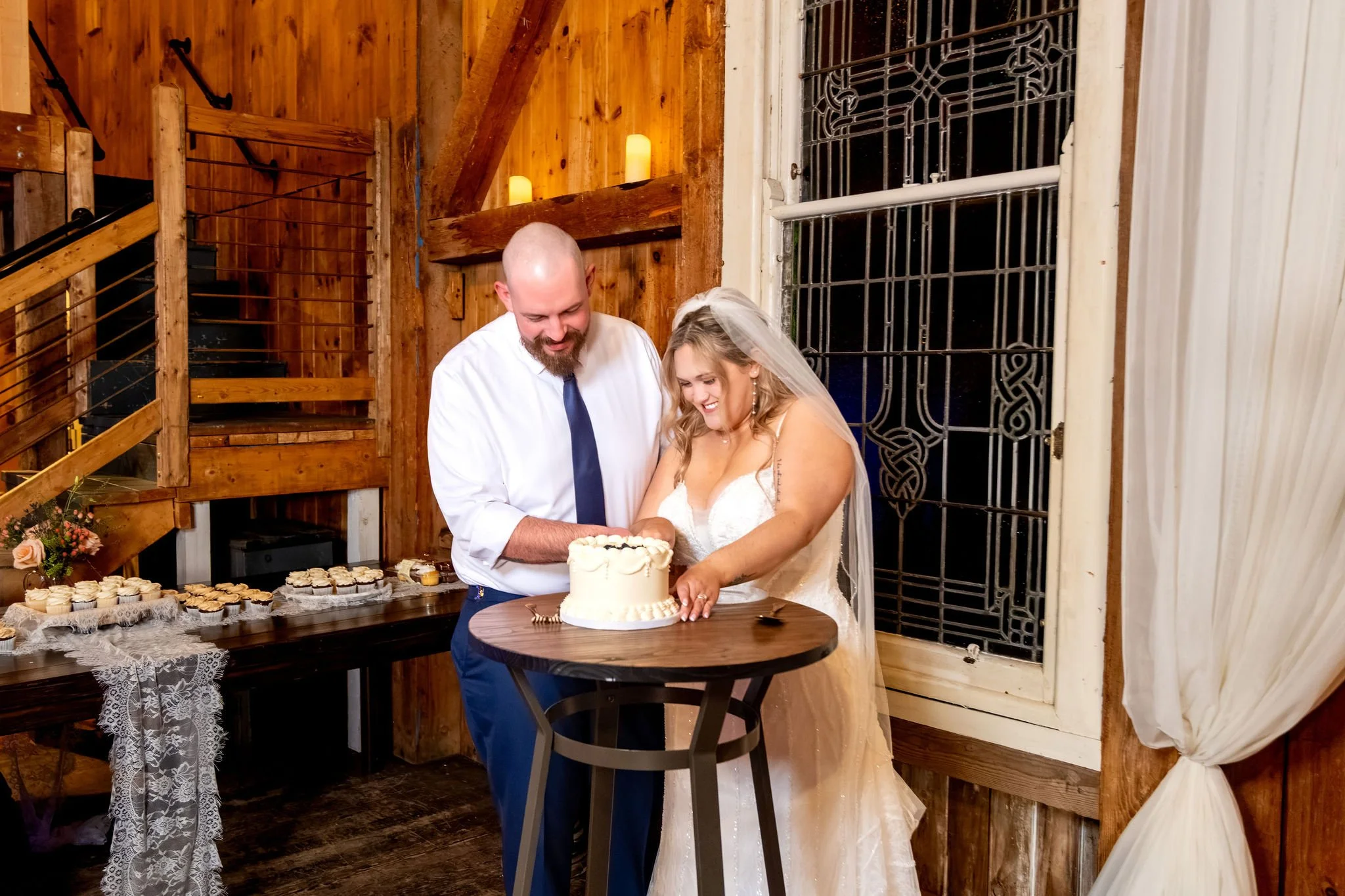 Ellie and Sam cutting their cake together at a round table with the cupcake display behind them at Boothbay Playhouse in Boothbay Maine fall wedding photography VMG Productions