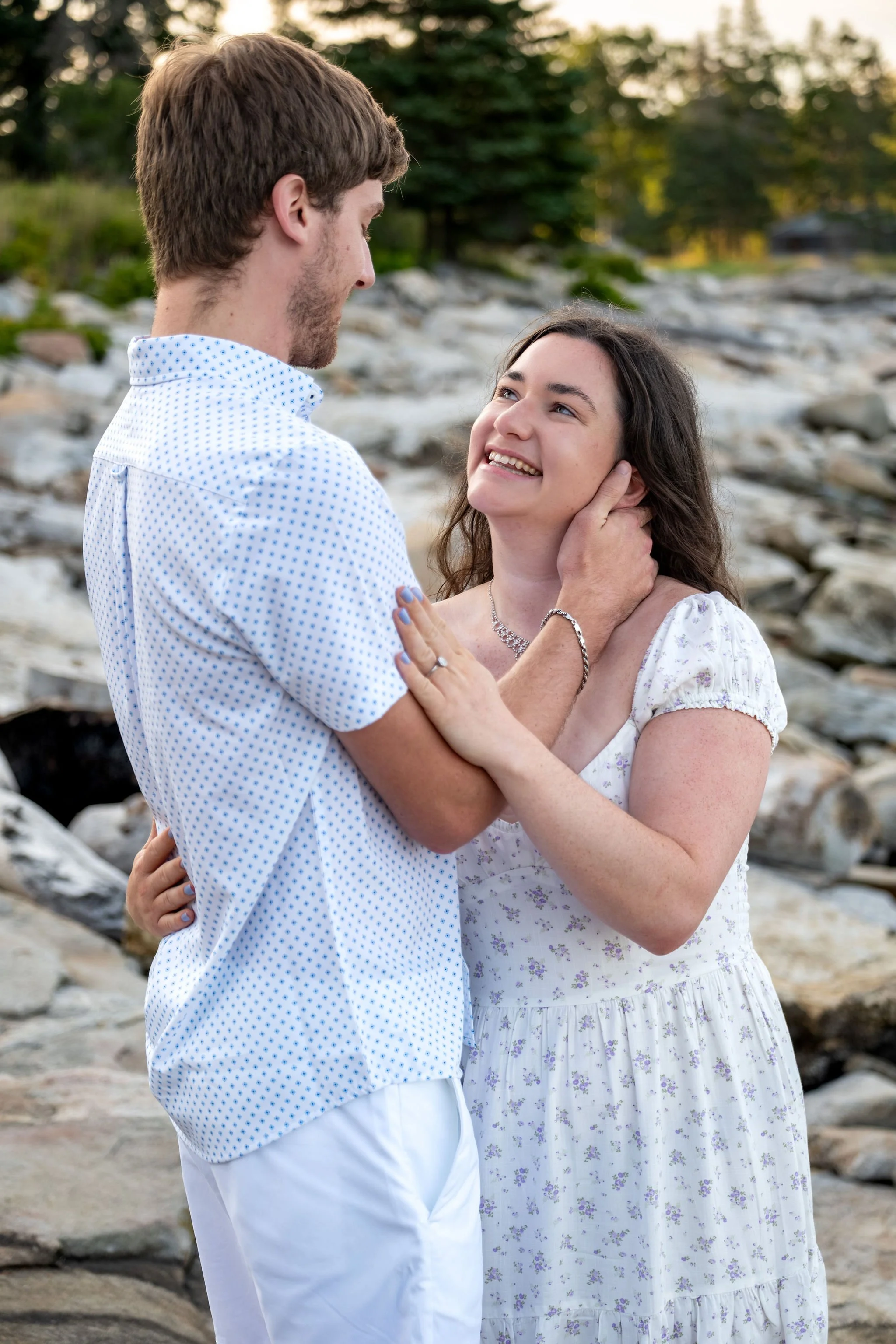 Kirstie with her hand on Lucas's chest looking up at him on the rocks at Reid State Park in Georgetown Maine engagement photography VMG Productions