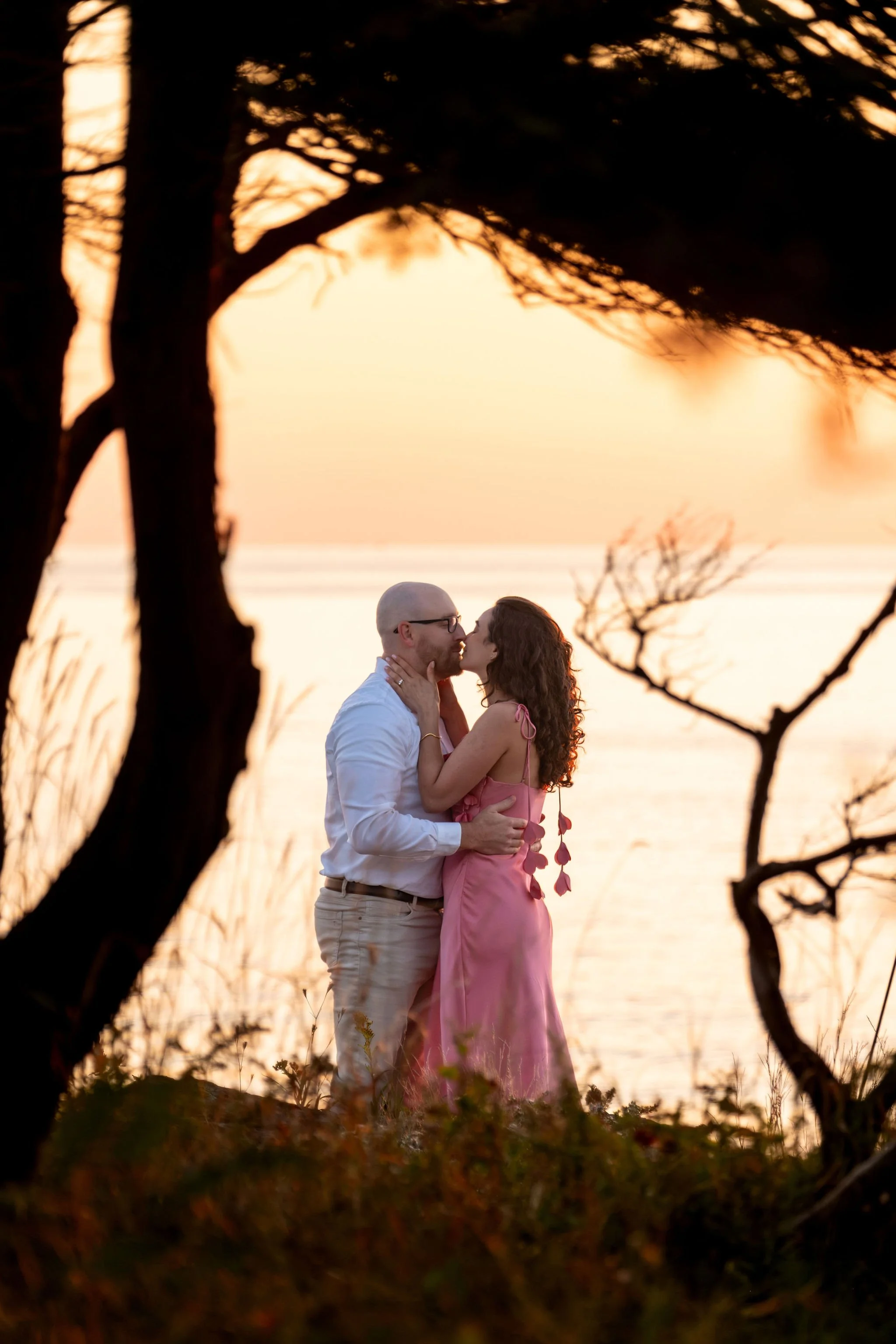 Zack and Helena sharing their first kiss as an engaged couple with the sunrise glowing behind them on Marginal Way in Ogunquit Maine sunrise proposal and engagement photography VMG Productions
