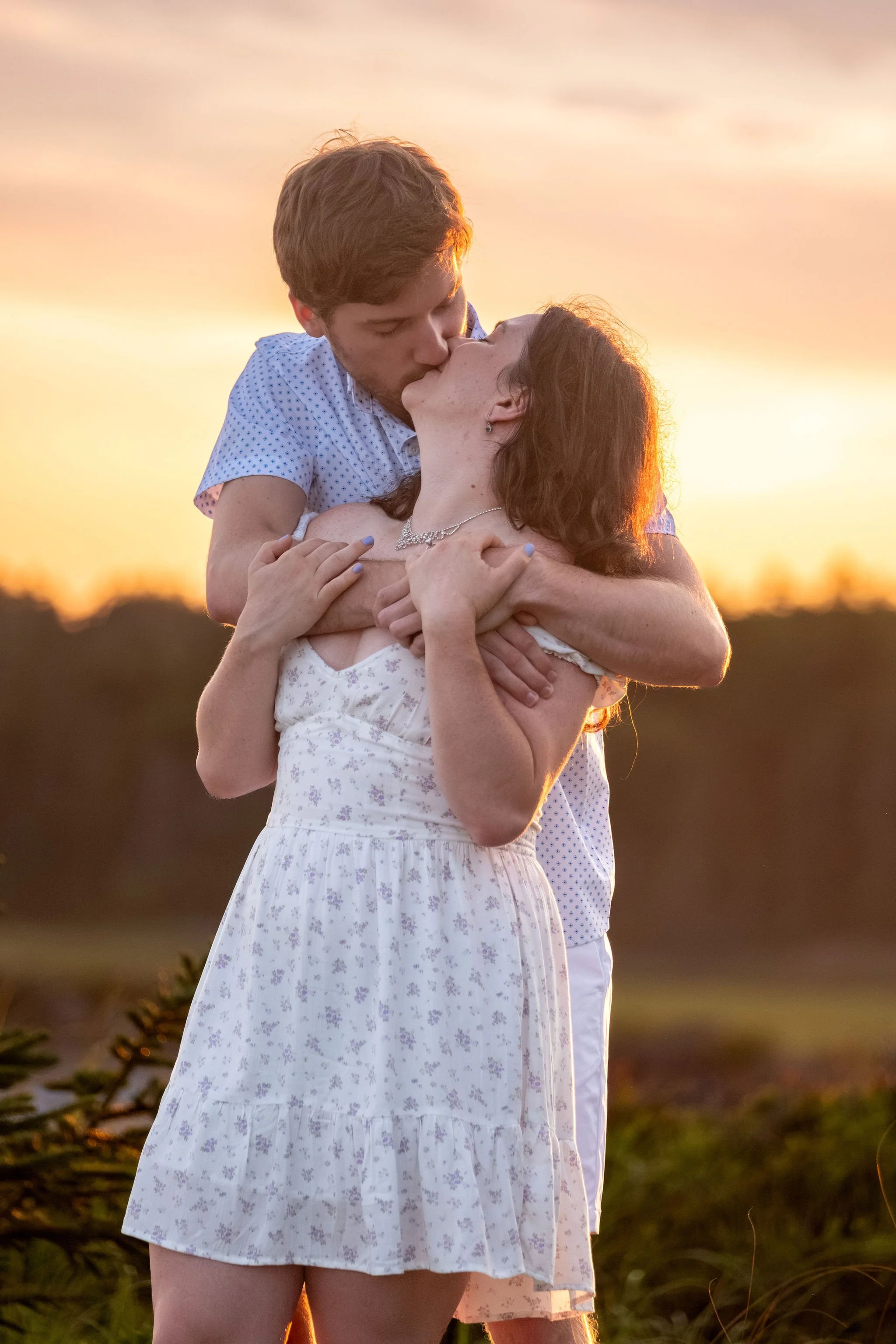 Lucas kissing Kirstie from behind with the golden sunset over the trees at Reid State Park in Georgetown Maine engagement photography VMG Productions