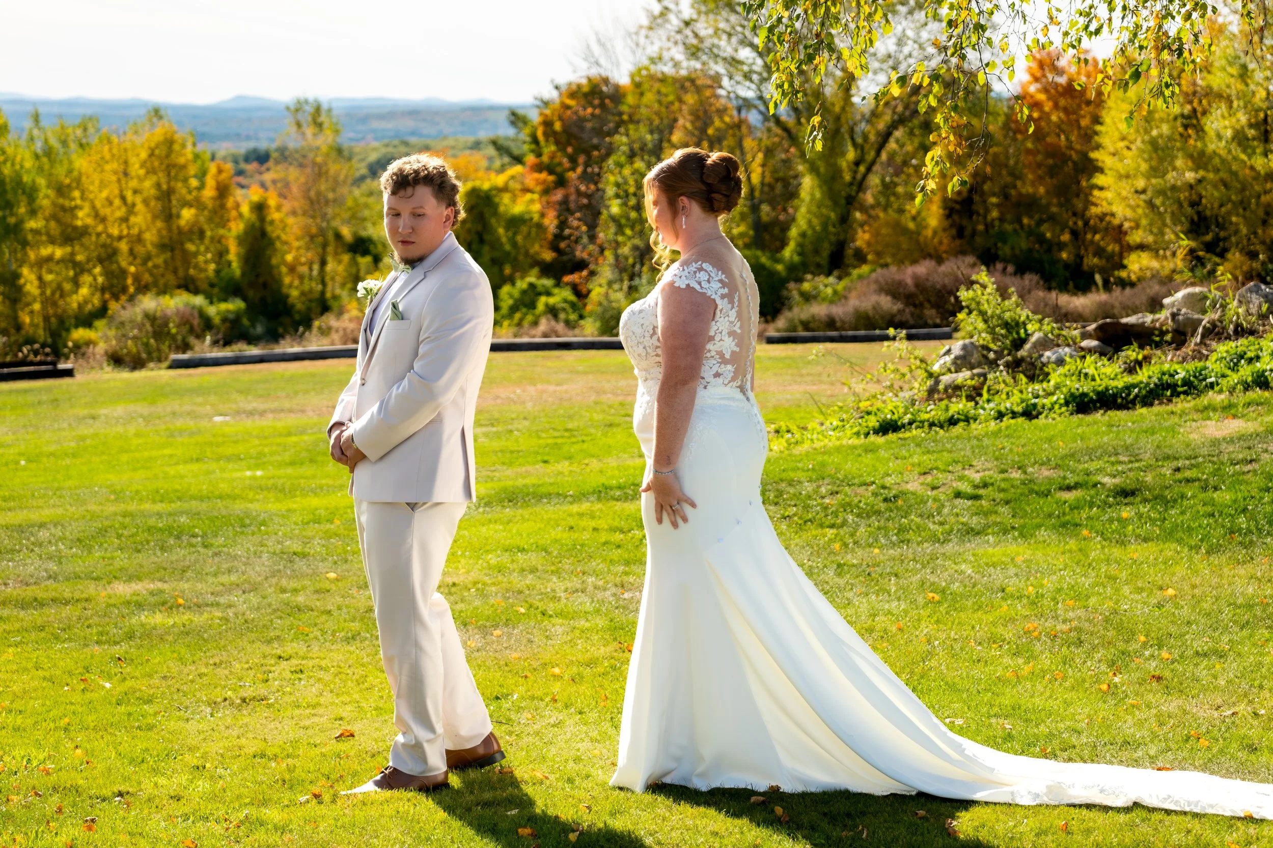 Andrew in his tan suit and Erika in her gown facing each other on the lawn before their first look at the Maine Wedding Barn and Event Center in Minot Maine fall wedding photography VMG Productions