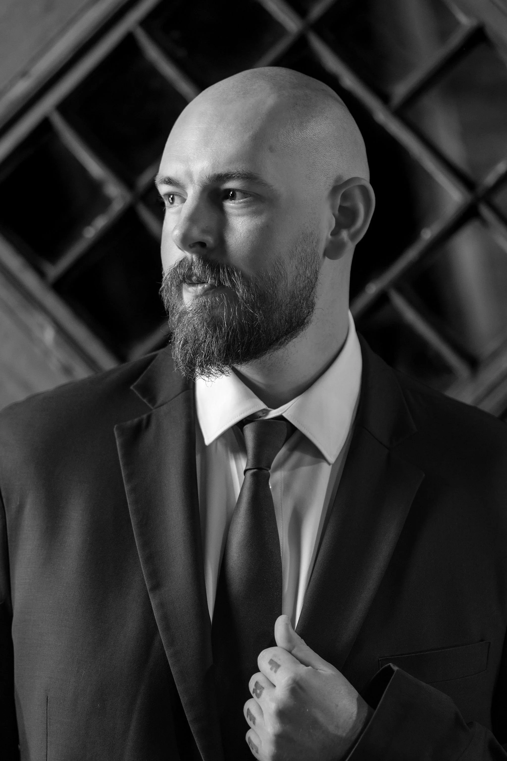 Black and white portrait of Sam in his suit looking off to the side against a lattice wall at Boothbay Playhouse in Boothbay Maine fall wedding photography VMG Productions